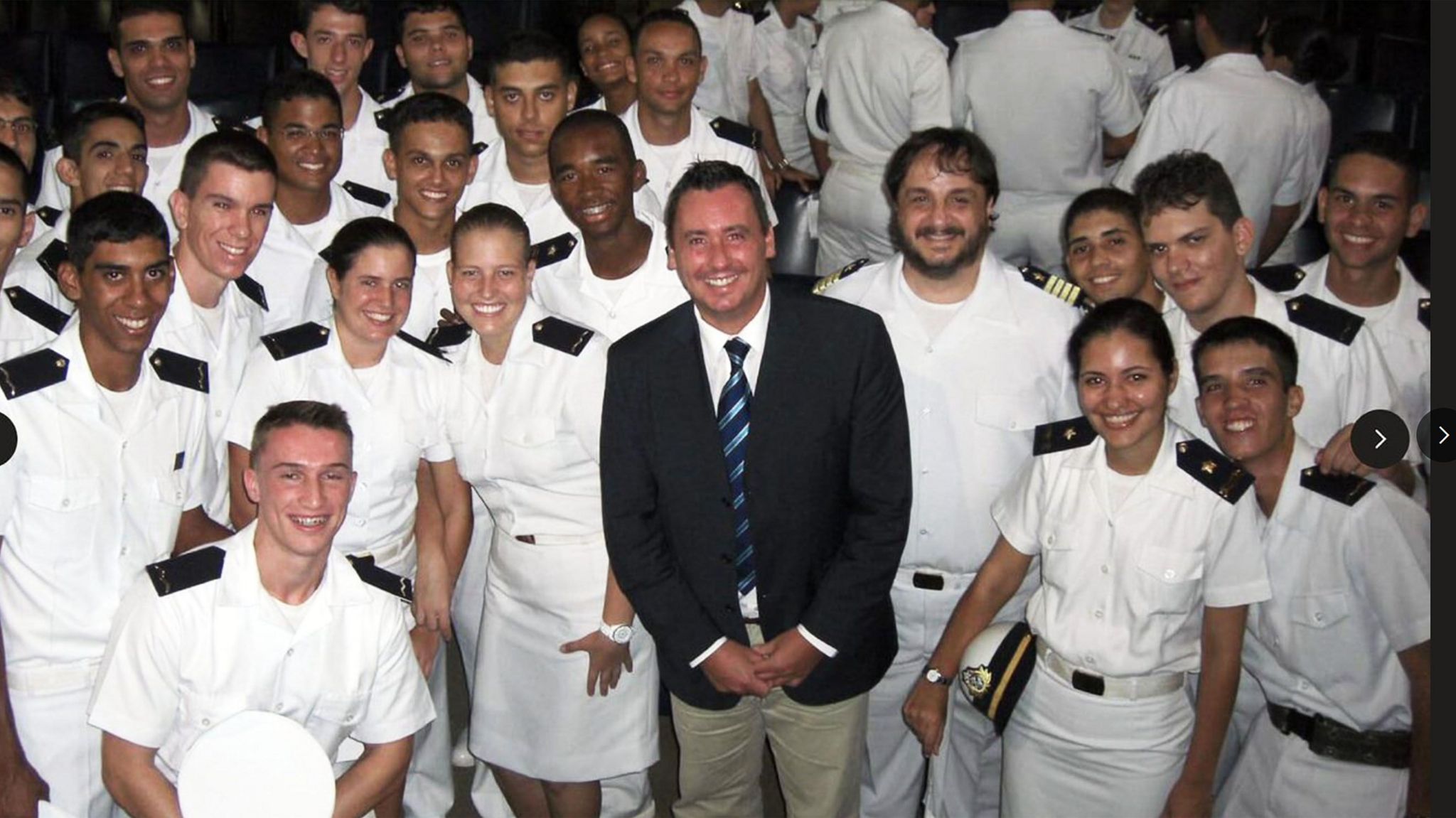 Steven Jones, in a blue blazer, white shirt, blue tie and grey trousers, stands amongst more than 20 Merchant Navy cadets, who are all wearing white uniforms