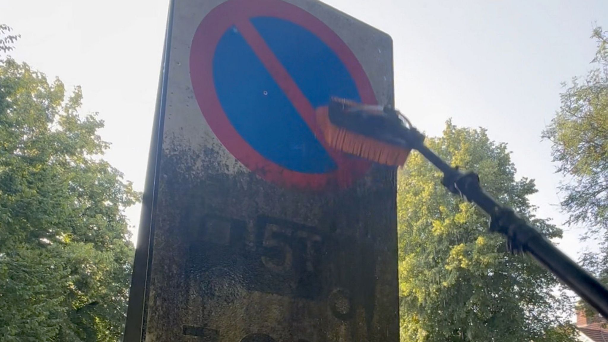 A dirty no waiting sign half cleaned by a pole-brush coming into shot from the right