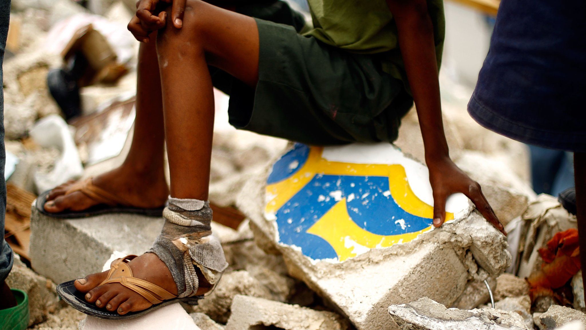 A young boy sits on a pile of rubble while watching others search a collapsed building for goods February 18, 2010 in Port-au-Prince, Haiti.