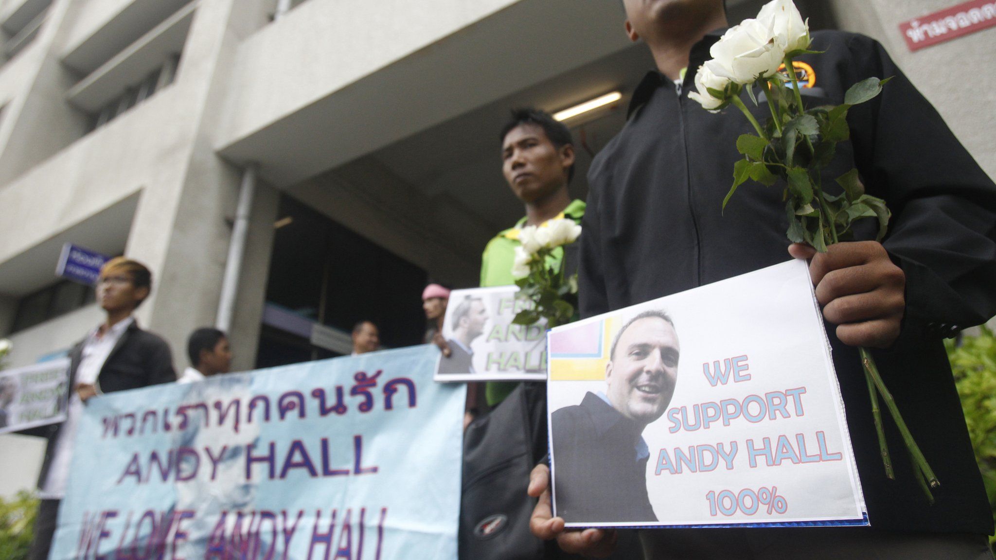 Supporters hold flowers and and placards as the British human rights activist Andy Hall arrives at Bangkok South Criminal Court
