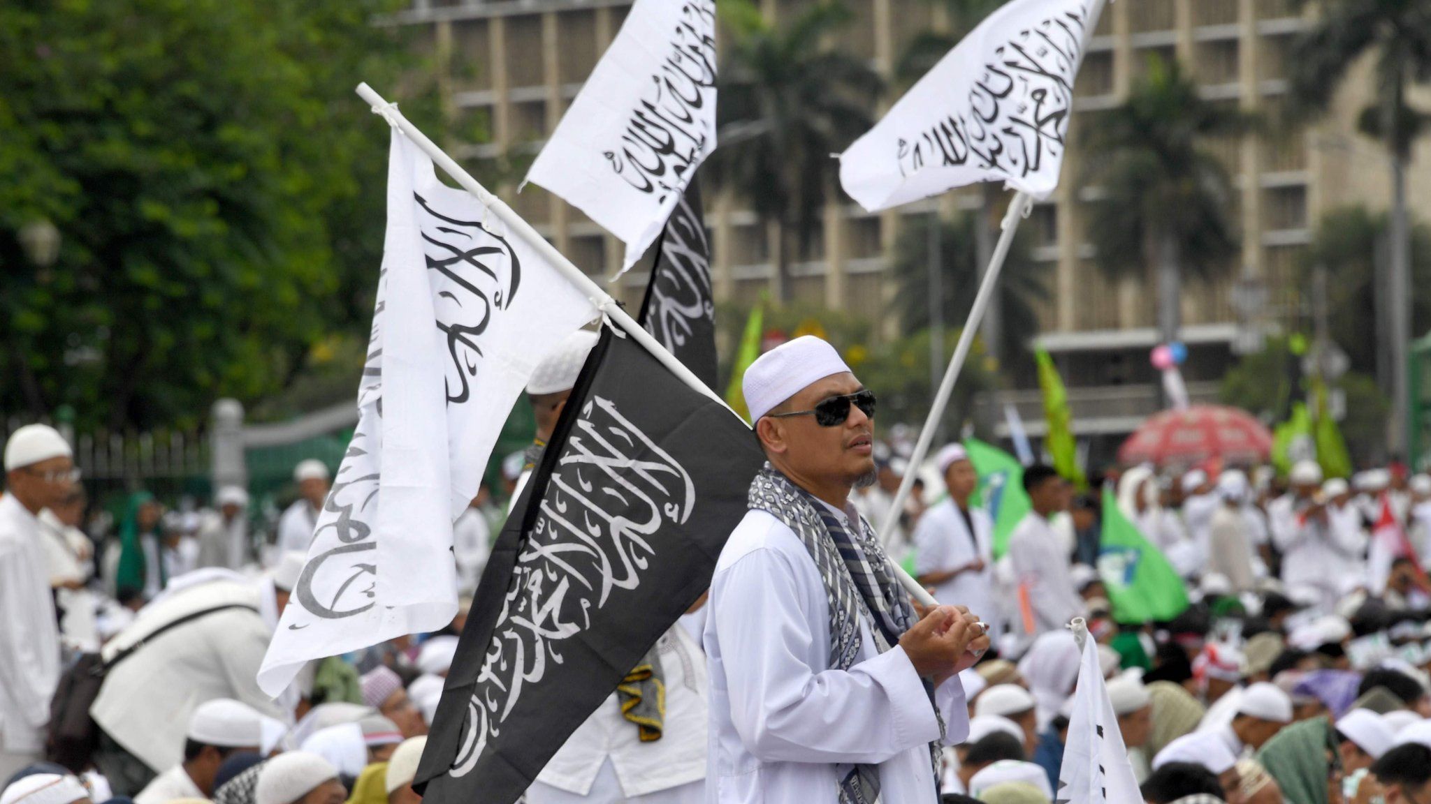 Indonesians in white Islamic robes gathered at Jakarta's National Monument park, with one standing and holding flags with Koranic verses on them. 2 December 2016.
