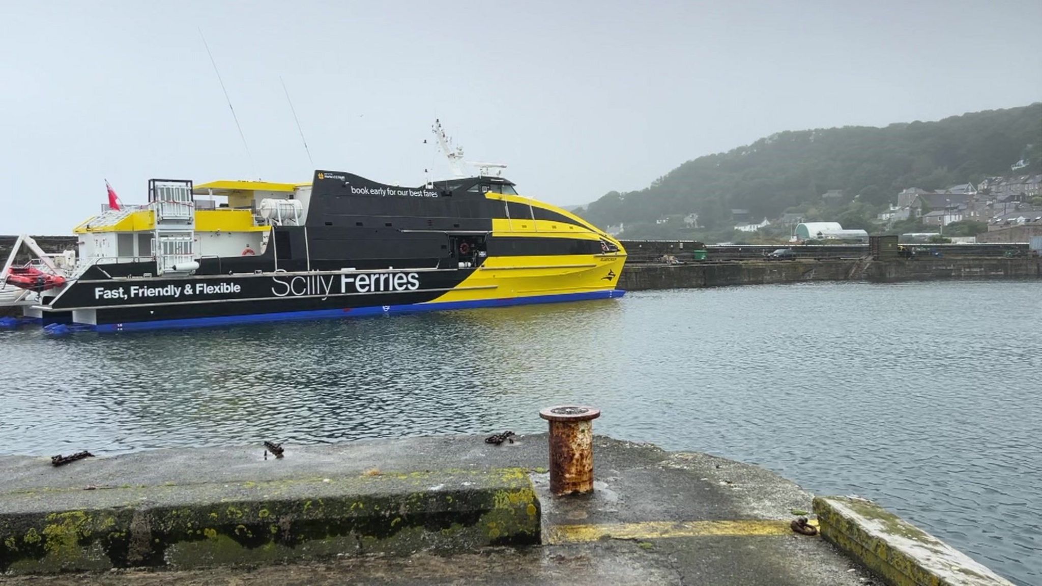 The Atlantic Wolff, a yellow and black ferry, at Newlyn harbour. It is on the water docked on a quay 