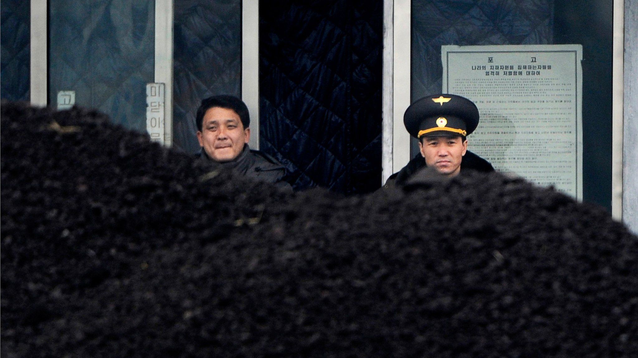 This file picture taken on 14 December 2012 from China's northeastern city of Dandong, looking across the border, shows a North Korean military officer (R) and a North Korea man (L) standing behind a pile of coal along the banks of the Yalu River in the northeast of the North Korean border town of Siniuju