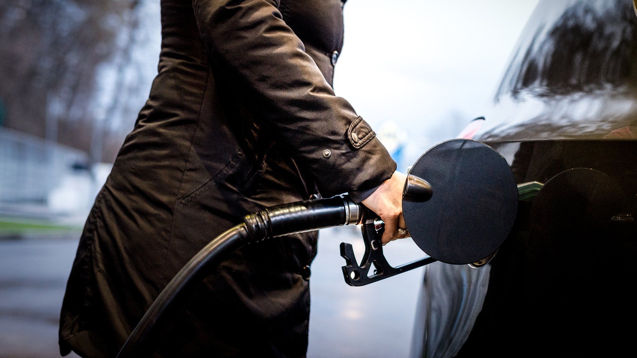 Woman wearing a coat filling up a car with fuel.
