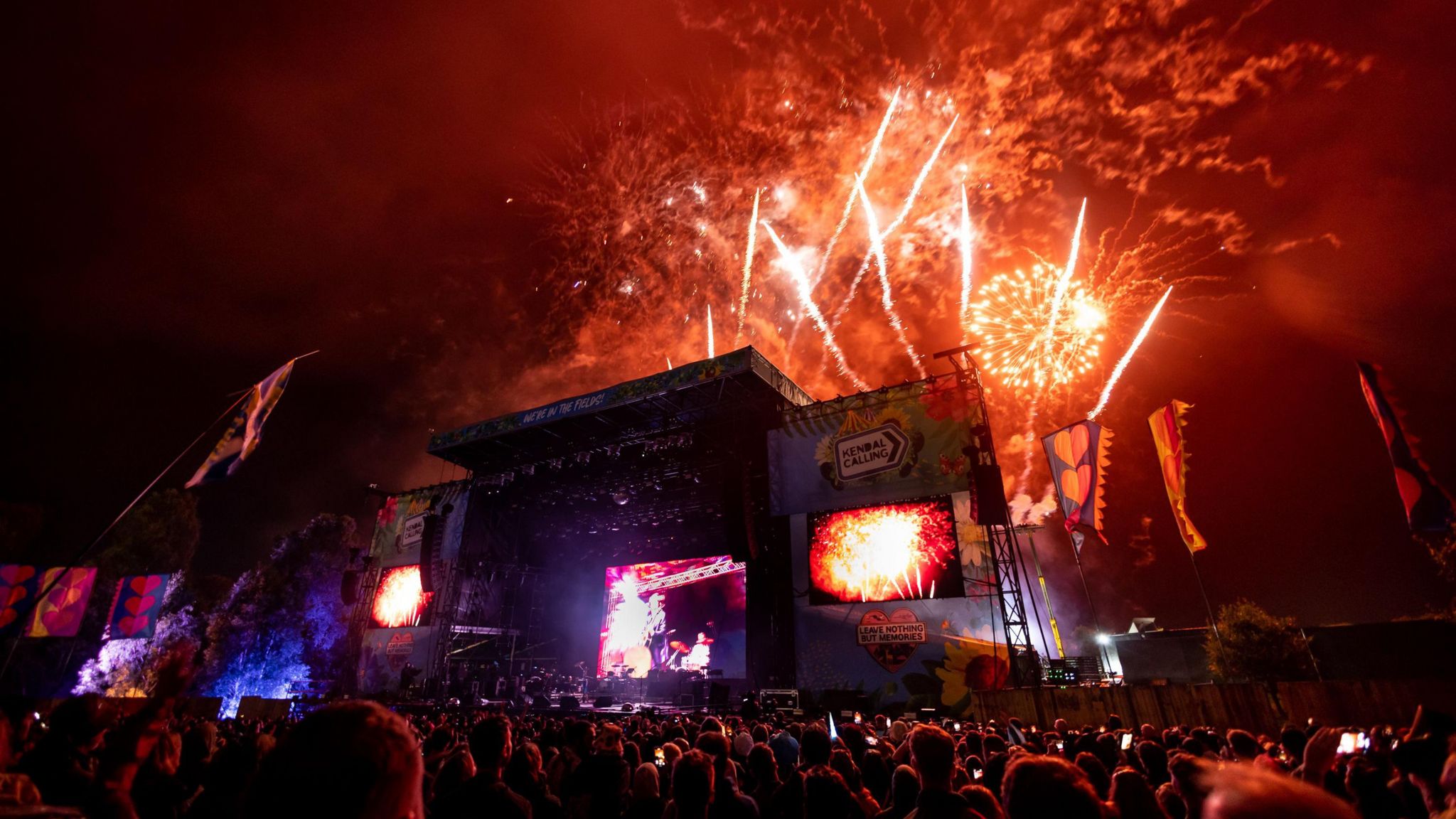 Orange fireworks light up the sky above Kendal Calling's stage with festival-goers watching.