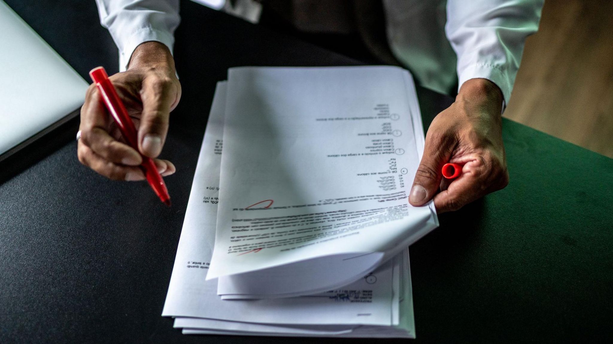 male hands holding white A4 paper with words printed on it. He has a red pen in one hand. There are some red markings on the page.
