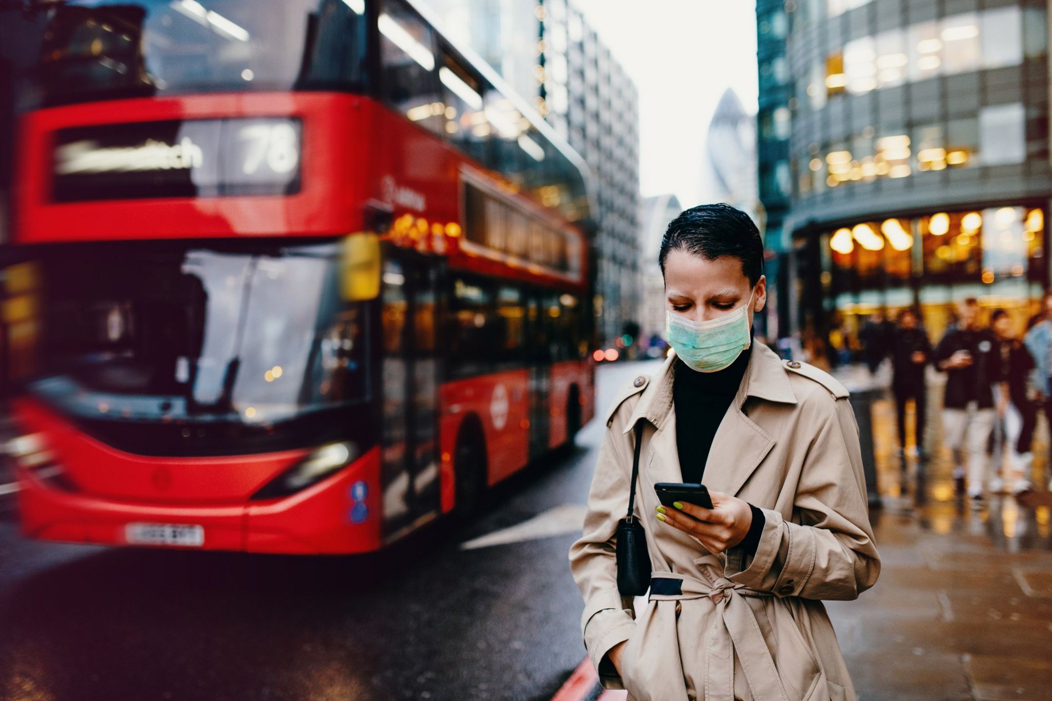 Woman waits by London bus stop in facemask