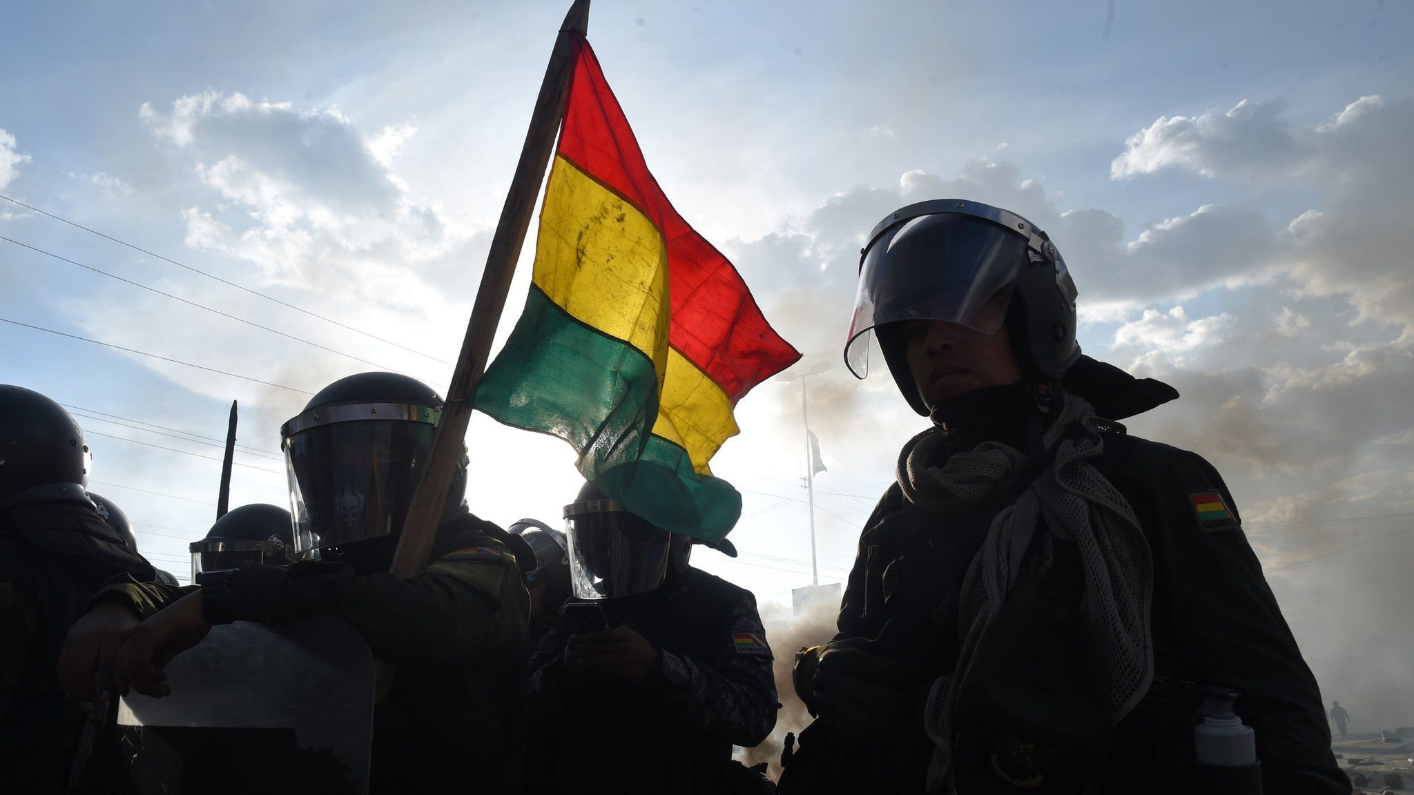 Shadows of riot police seen in Sacaba, with a Bolivian flag