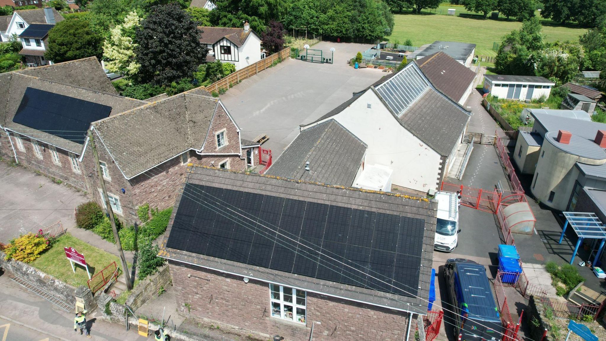 Aerial view of school with solar panels on two buildings and cars parked nearby.