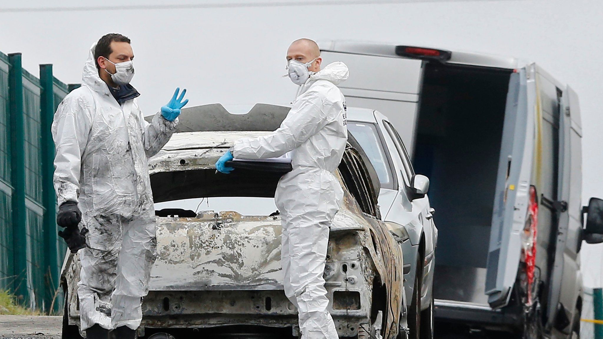 French police officers search through the burnt-out cars