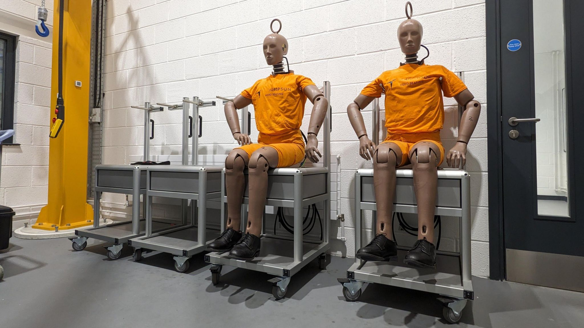 Crash test dummies sit on trolleys wearing orange jerseys.