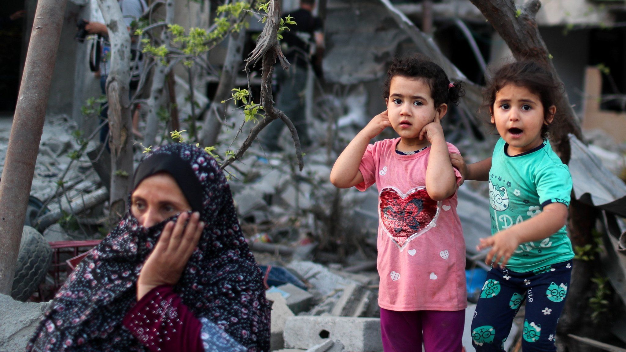 A Palestinian woman sits as two girls stand near destroyed houses in the northern Gaza Strip (1 June 2021)