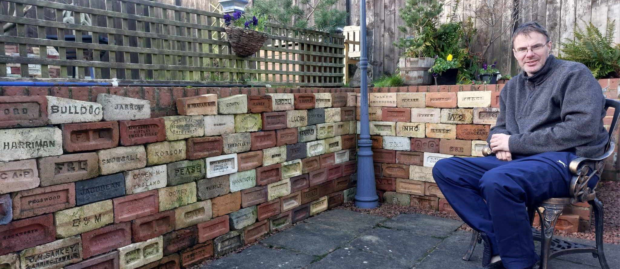 Mike Graham sitting by a wall of his collected bricks