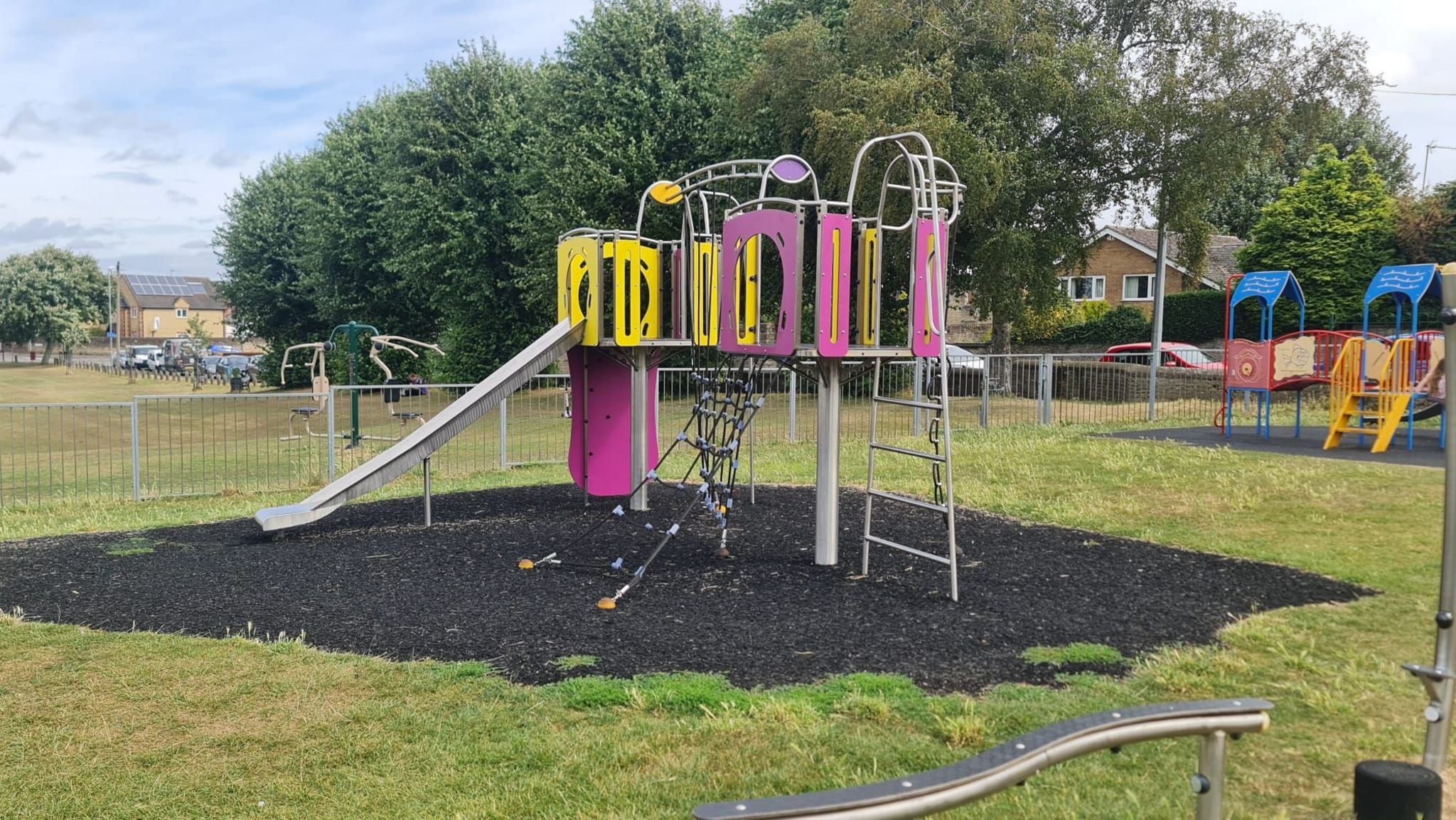 A slide, a pink climbing frame and a silver balance beam in the middle of a grass area