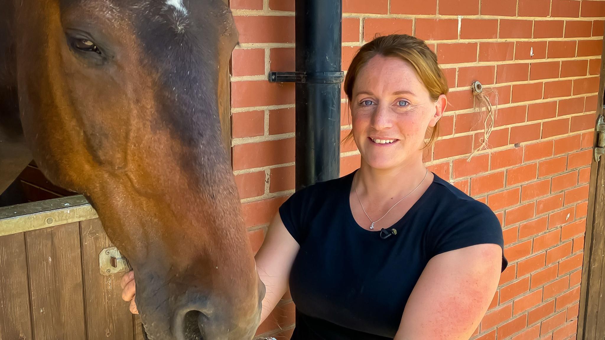 Woman in a black shirt next to a horse in a barn