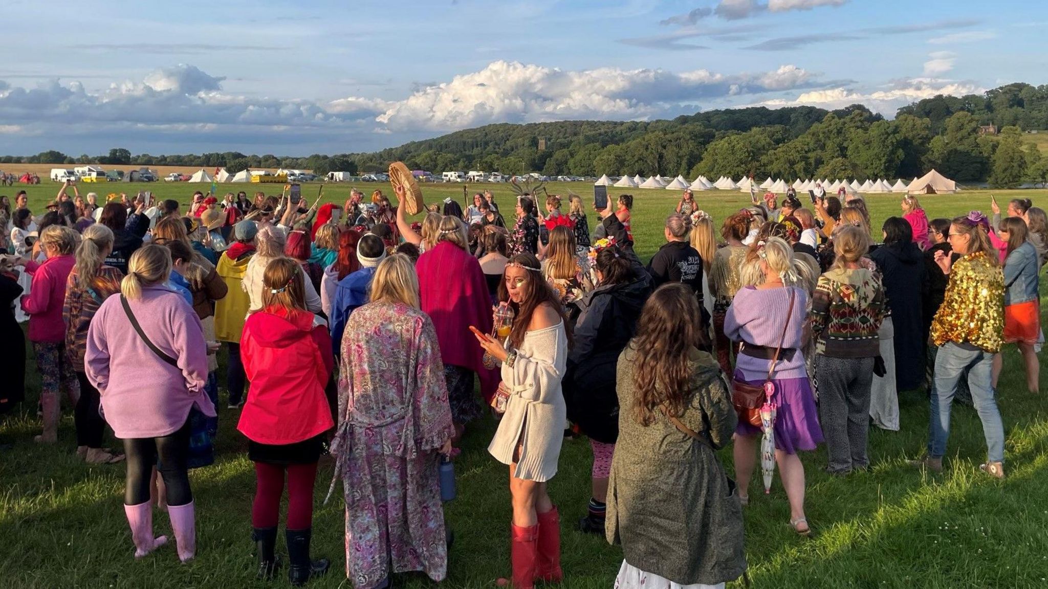 Women revelling on a field with teepee-style tents in the far distance