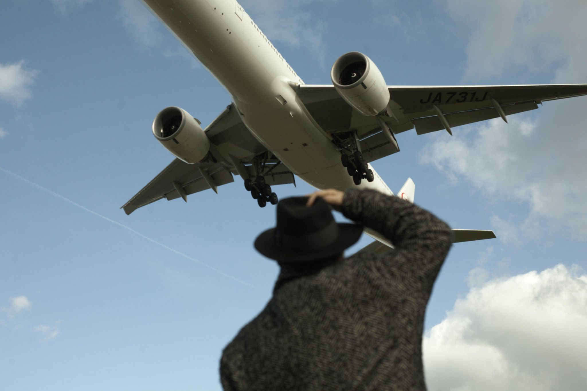 Man holds onto hat as plane flies overhead