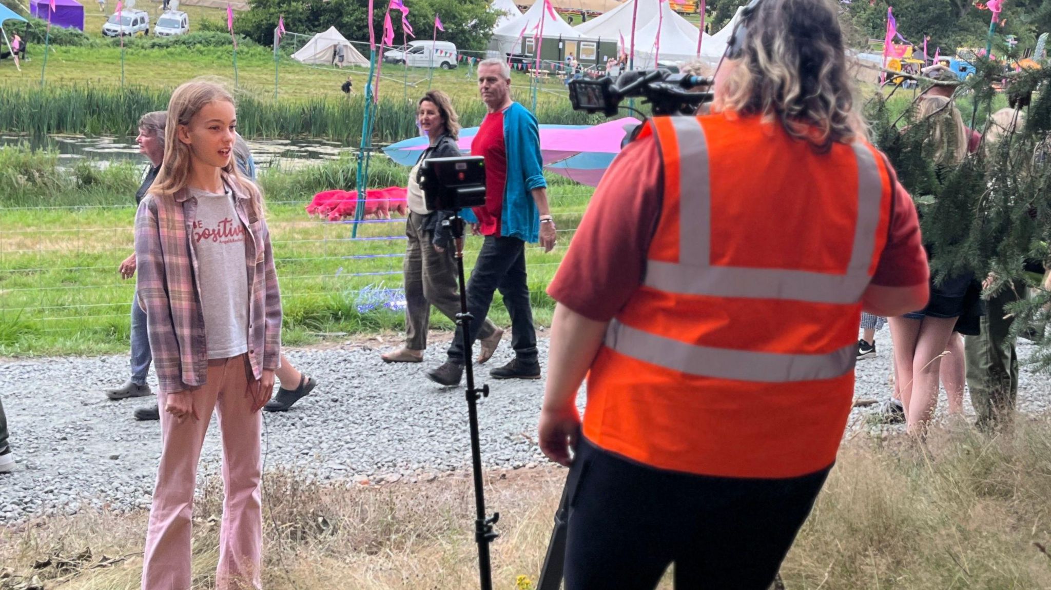 Anna stands in front of a TV camera with Latitude pink sheep in the background