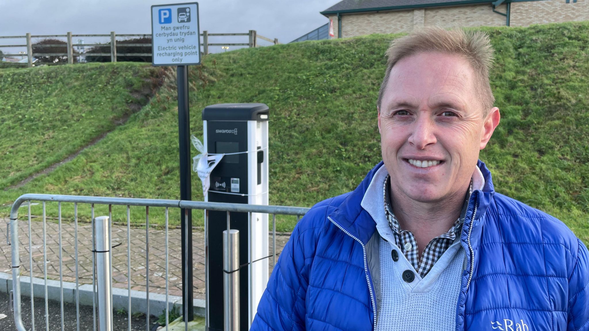 EV driver Aled Jones stands by one of the unconnected charge points in Caernarfon, with a barrier between him and the EV point