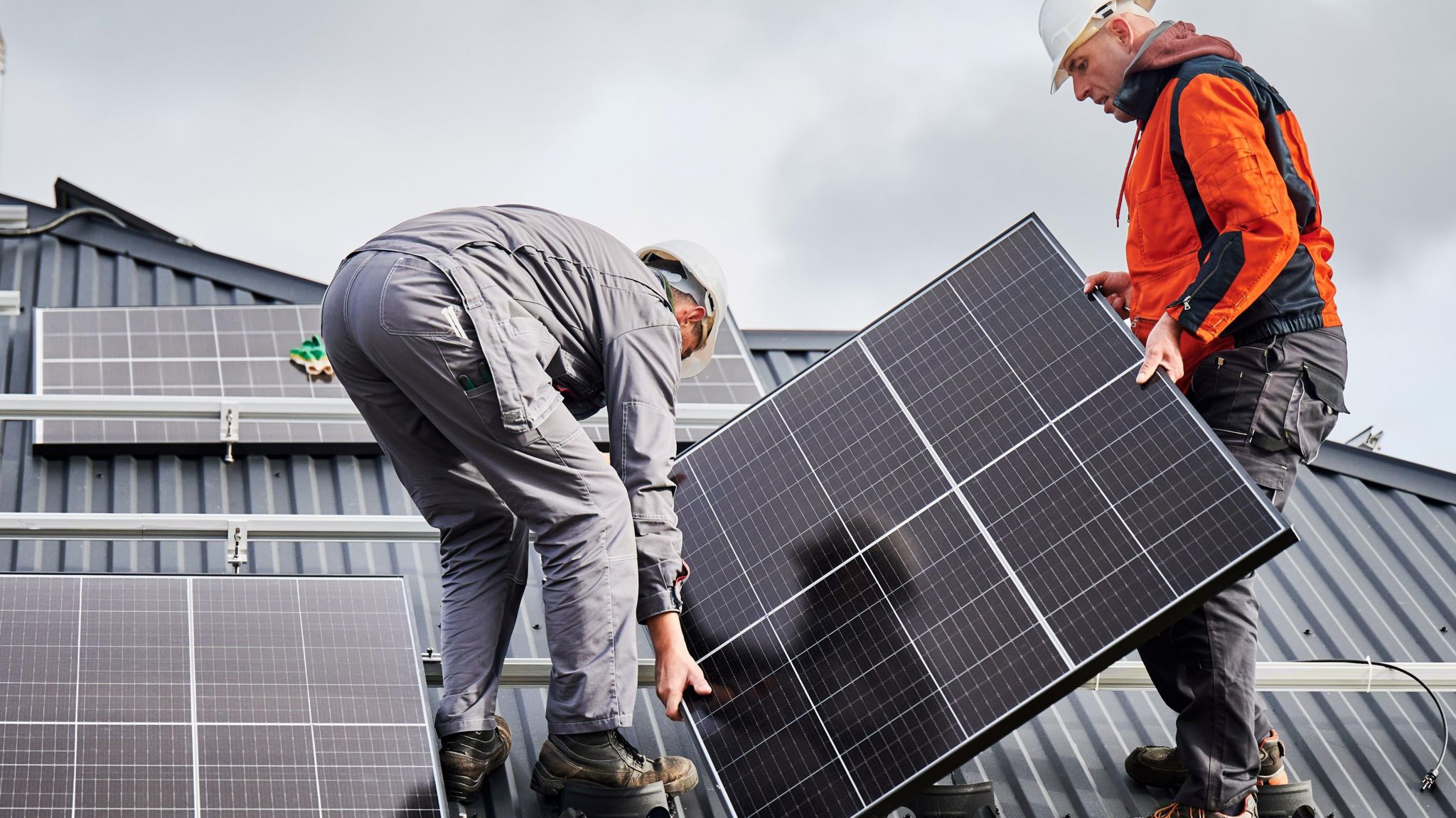 Two workmen installing solar panels on a roof