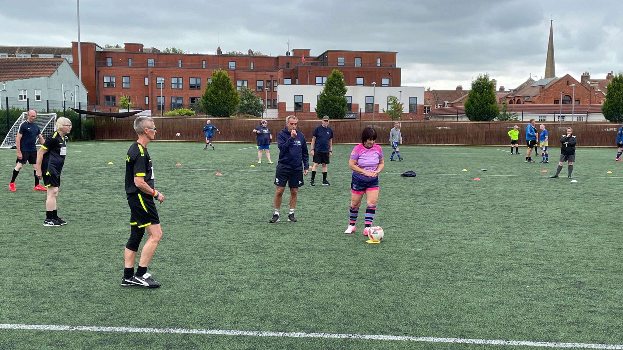 Walking football players on the pitch wearing black and pink kits.