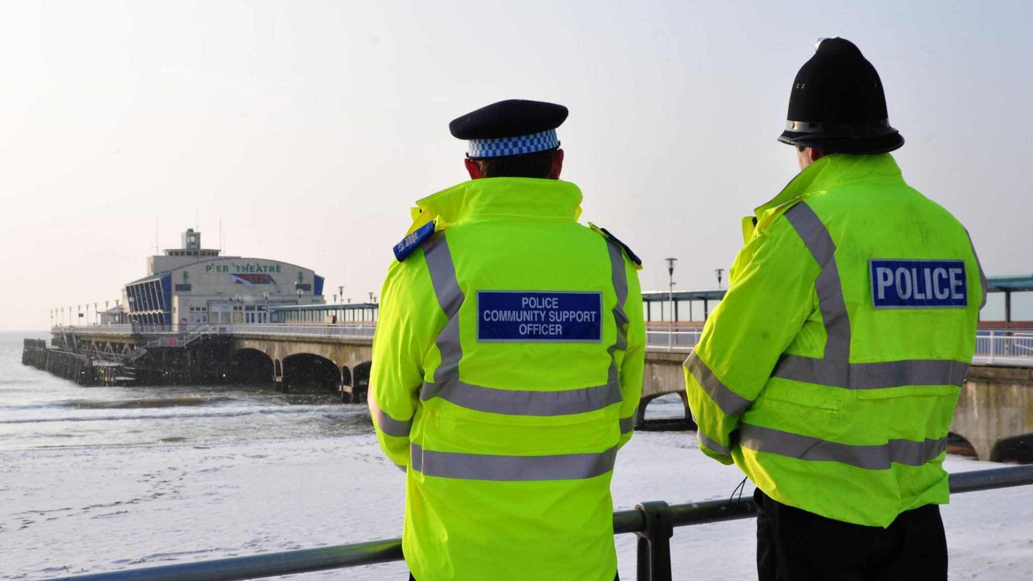 Two police officers standing by a railing looking out over the sea. Bournemouth Pier is in the background.