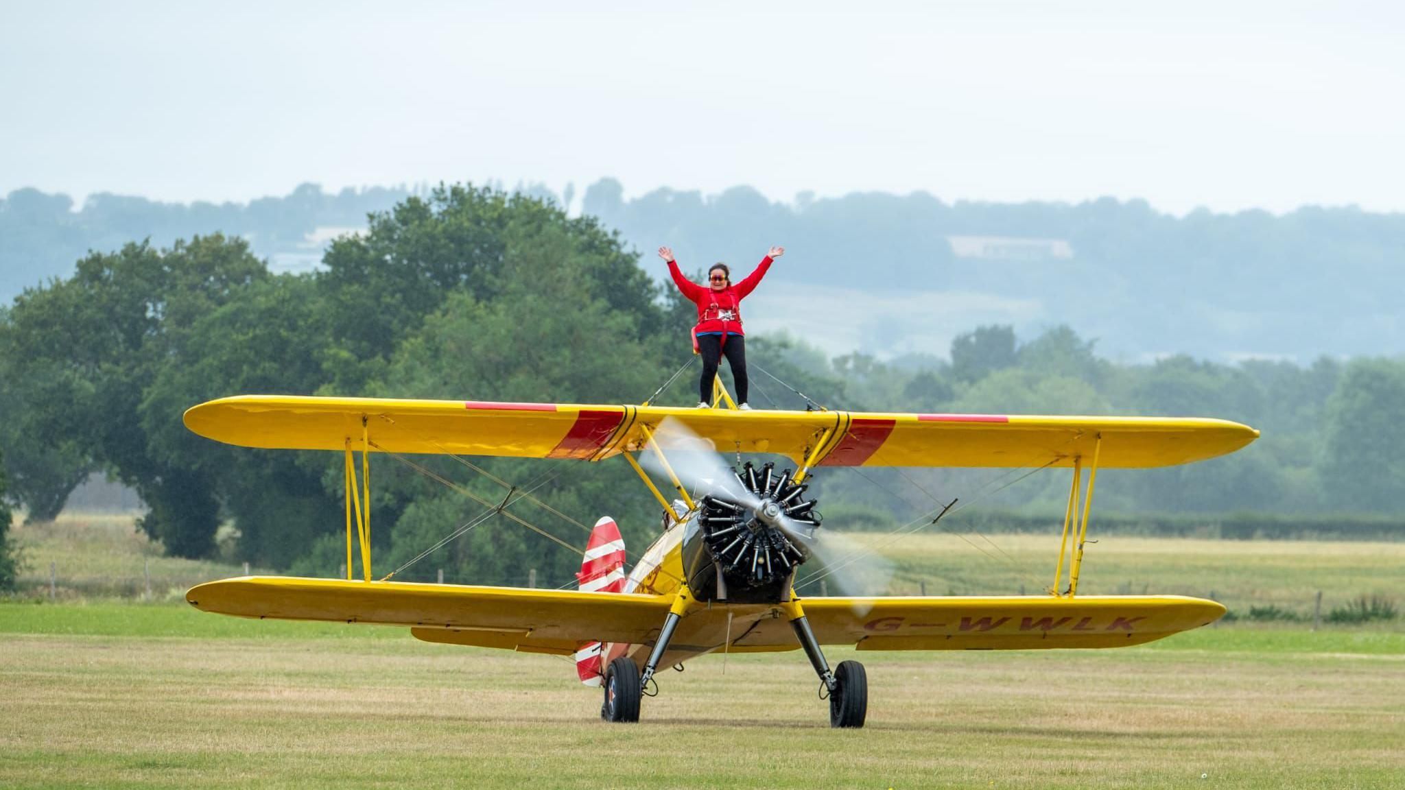 Suzanne Gratton, 80, standing on a Boeing Stearman plane 