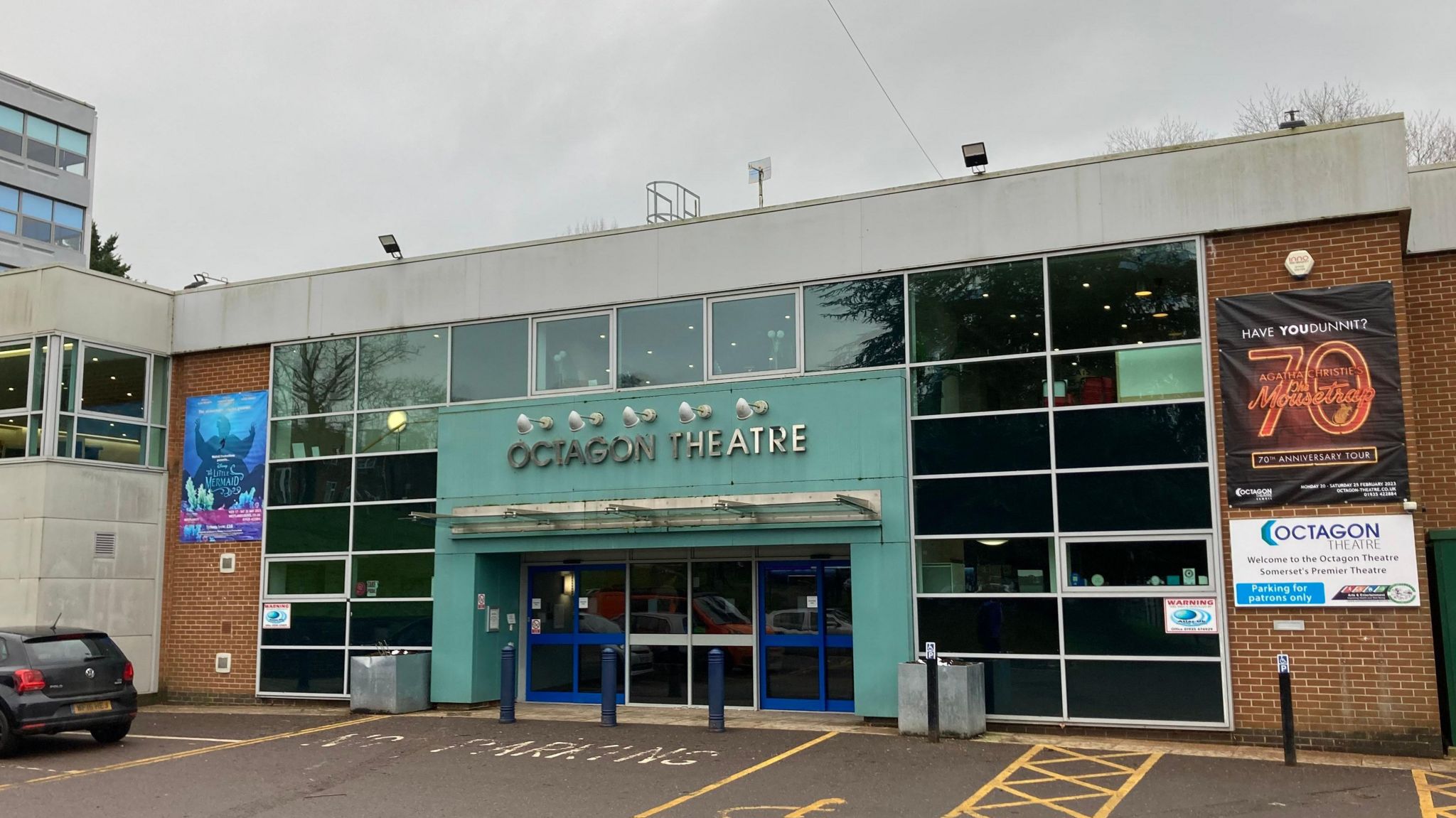 Octagon Theatre in Yeovil, which is a brick building with large glass windows at the front. The doors are surrounded in green with the words Octagon Theatre above them. 