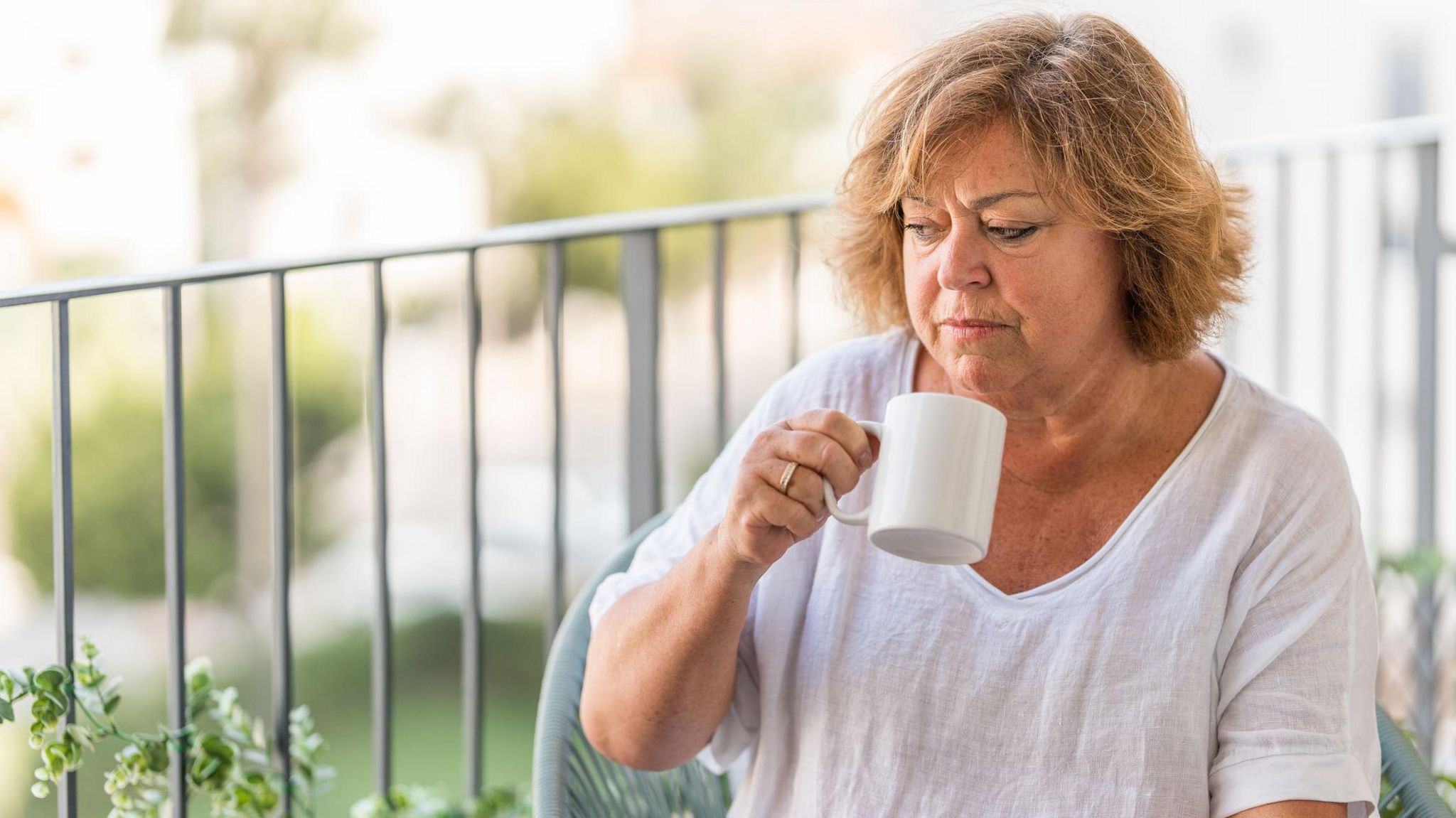 Woman in her 60s sits on a balcony drinking a cup of tea