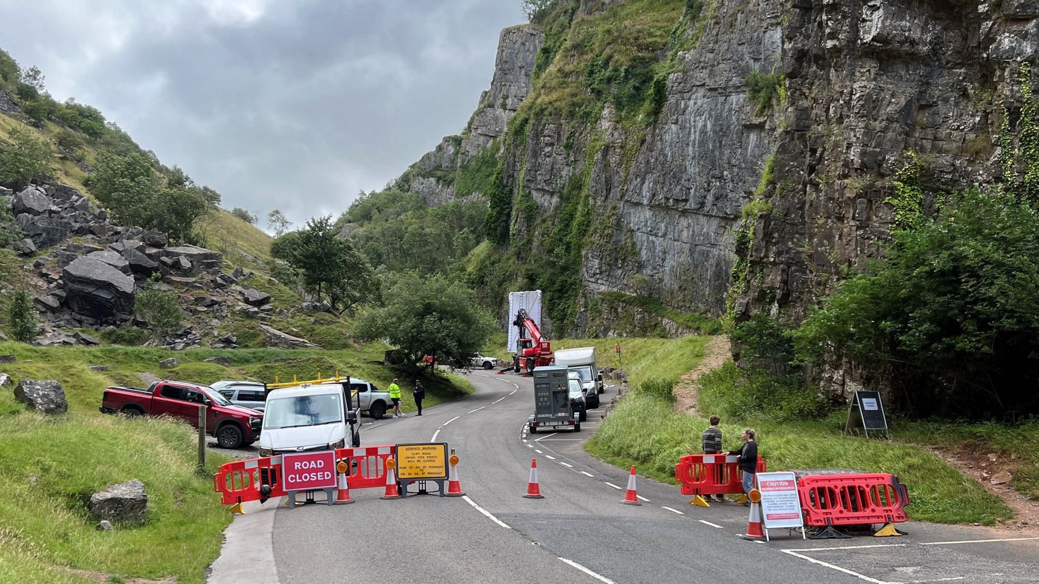 A road going through Cheddar Gorge with closed signs and red warning cones with filming equipment in the distance