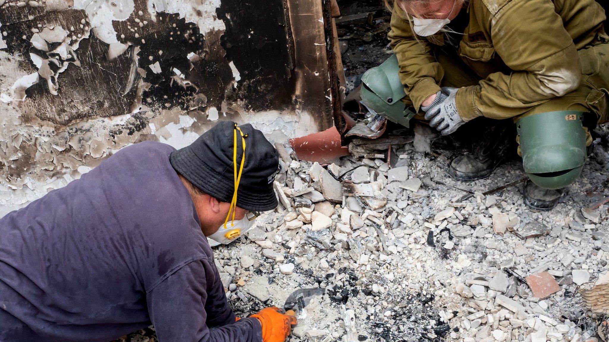 An Israeli archaeologist and two soldiers inspect charred debris on the floor of a house in southern Israel that was set on fire during Hamas's attack on 7 October