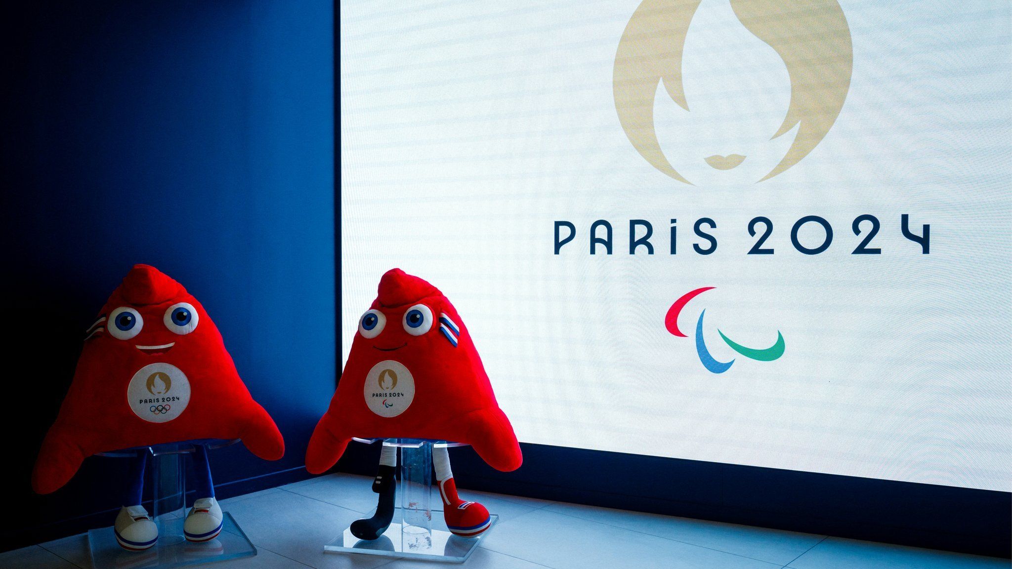 The Paris Olympic and Paralympic mascots in front of the Paralympic logo