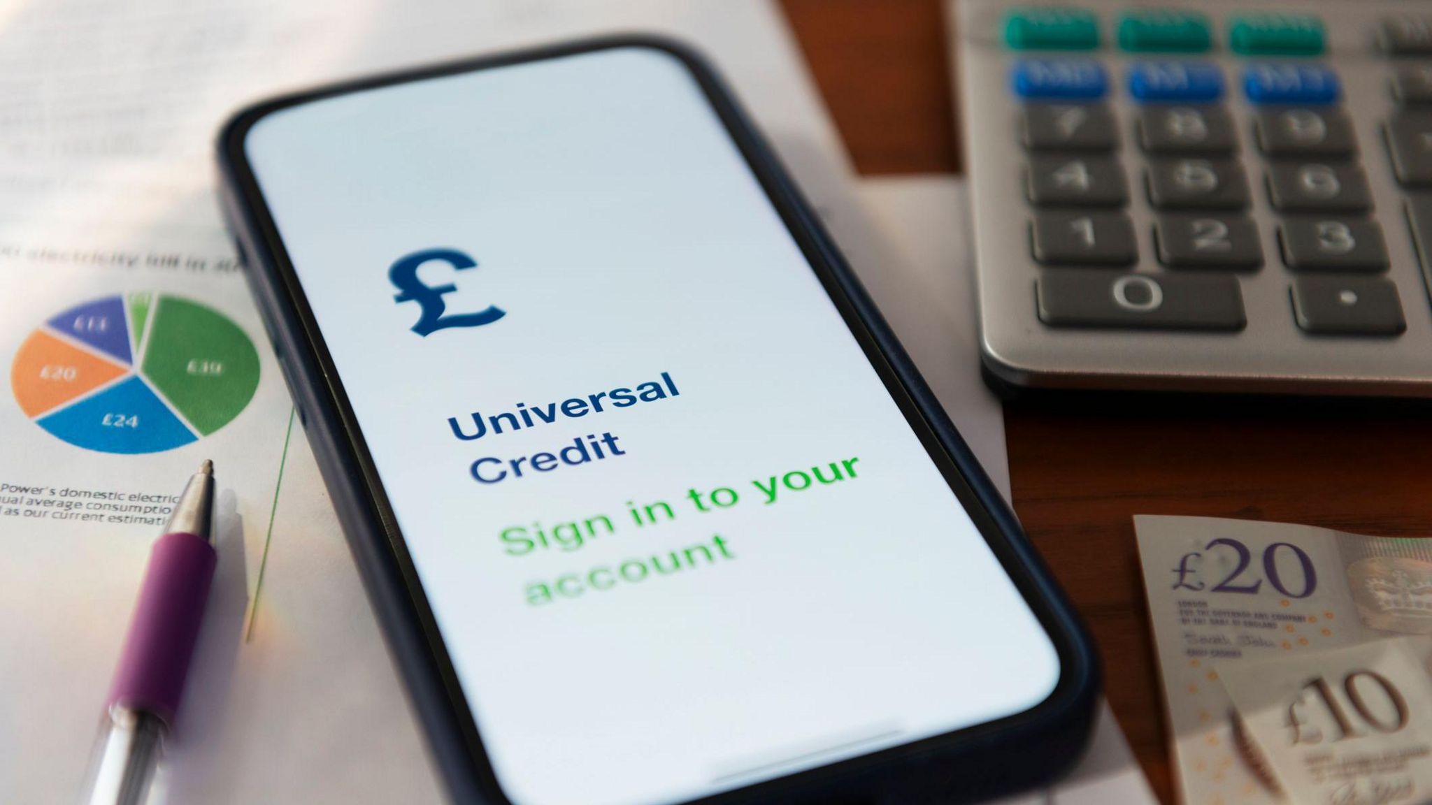 A smart phone open on a Universal Credit sign in page next to a calculator and some bank notes