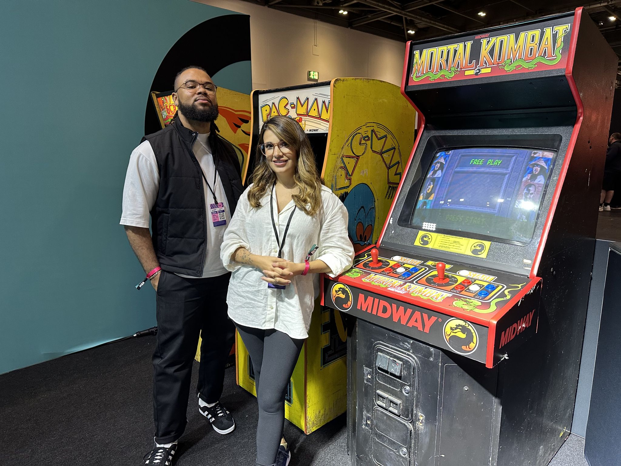 A man in a gillet and a woman in a white shirt stand in front of arcade machines