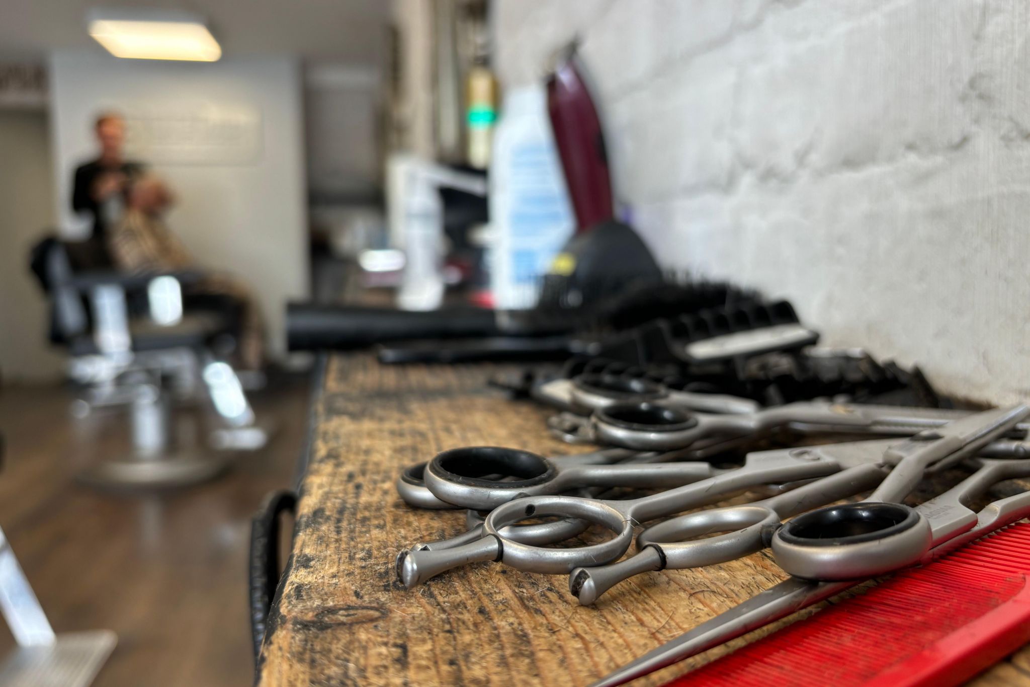 A close-up of scissors and a comb, sat on a table inside Leon Ball's barber shop, with two people out of focus in the background