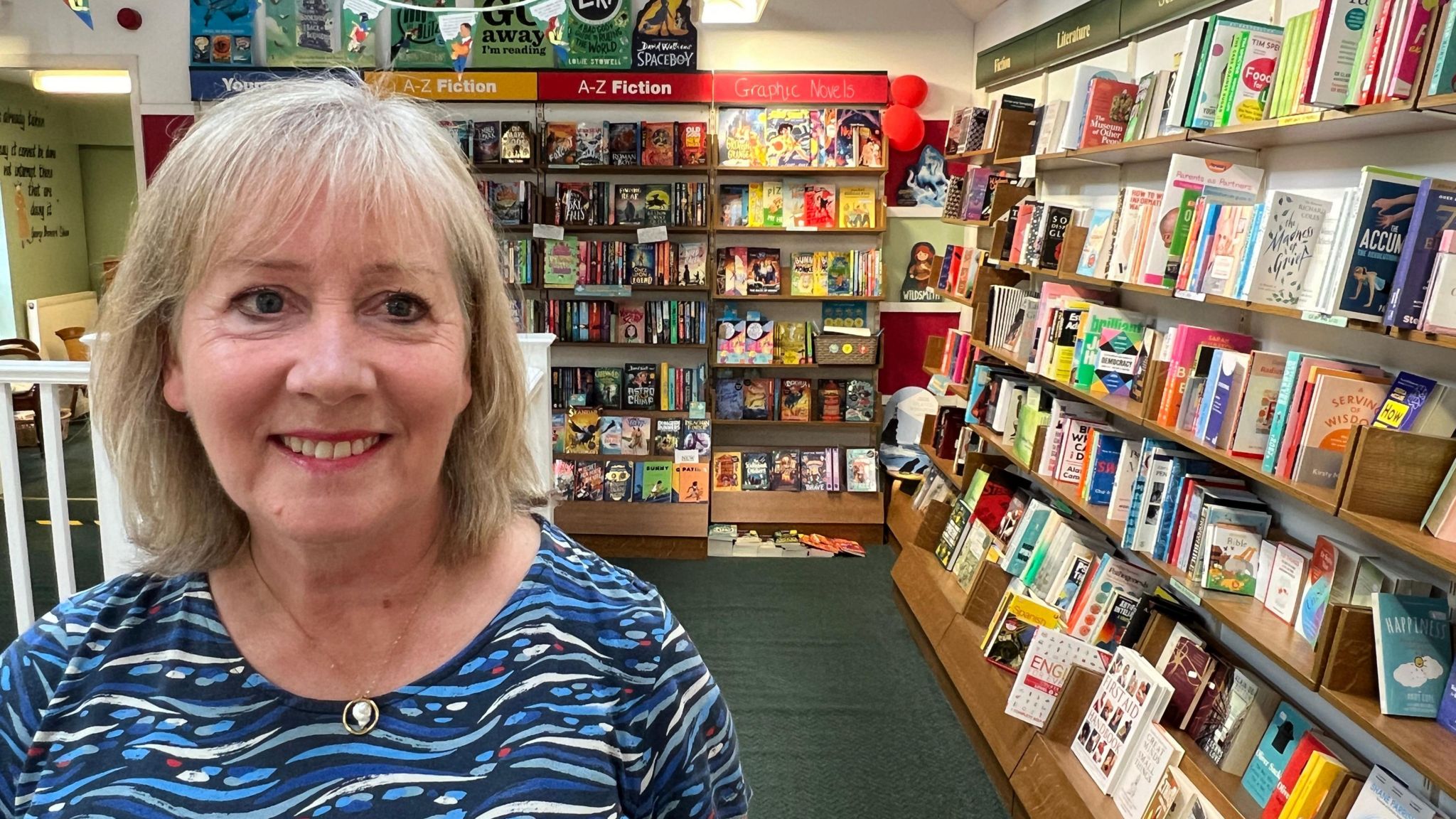 White Rose Book Cafe owner Sue Lake - wearing a patterned blouse - pictured in her Thirsk book shop