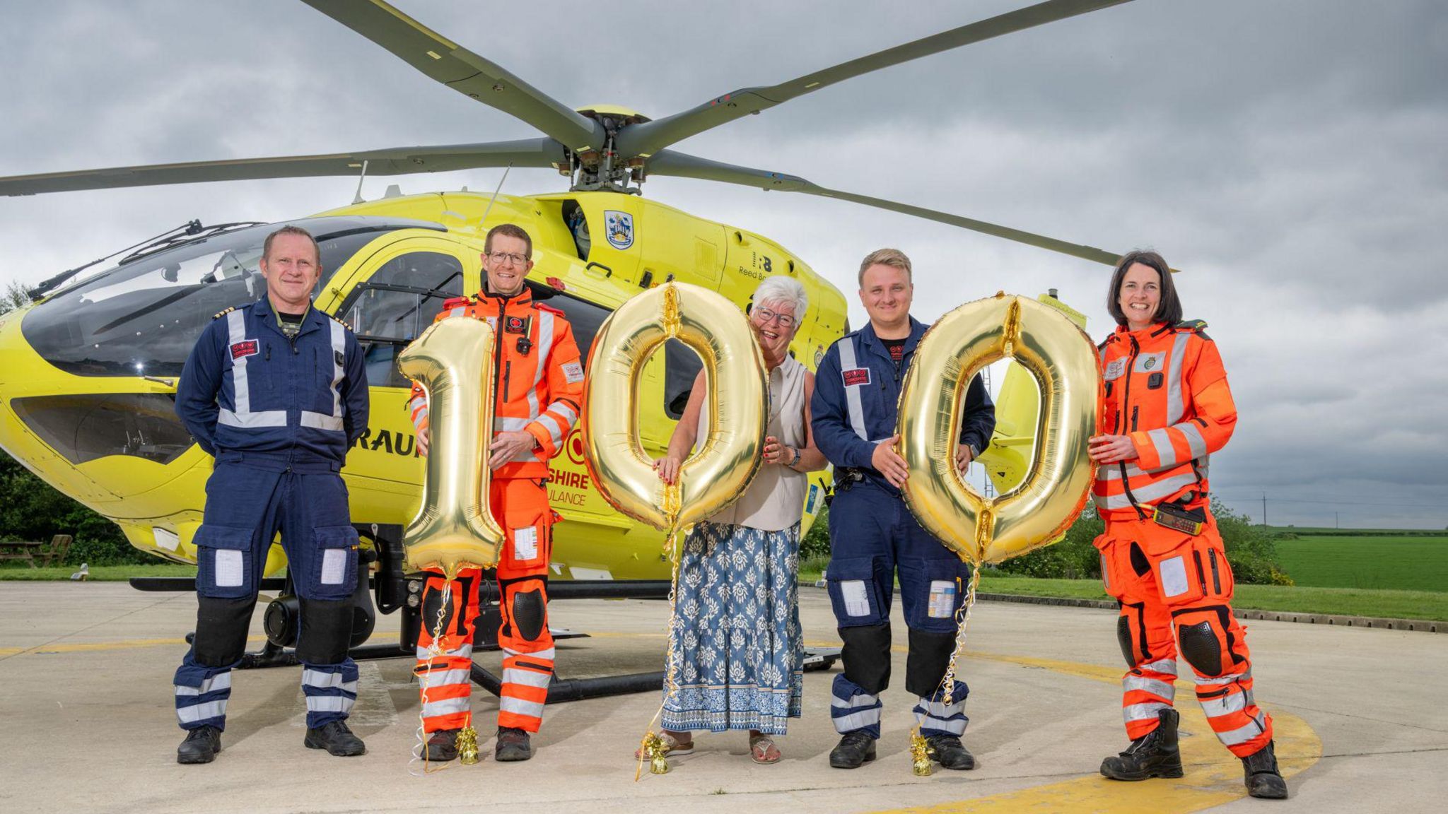 Janet Swallow stands with Yorkshire Air Ambulance crew and 100 balloons in front of a helicopter