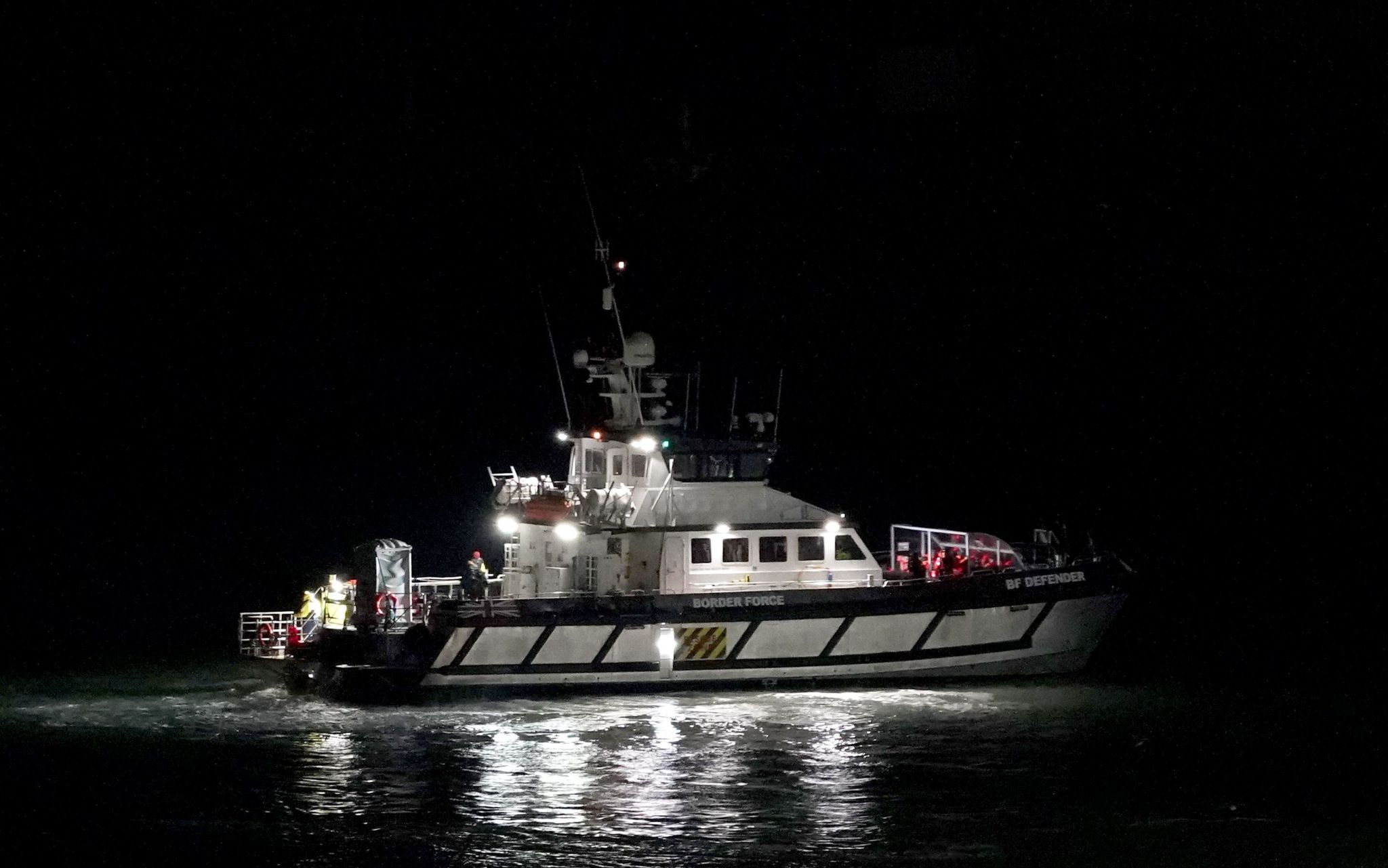 A black and white Border Force boat with lights beaming out in the dark
