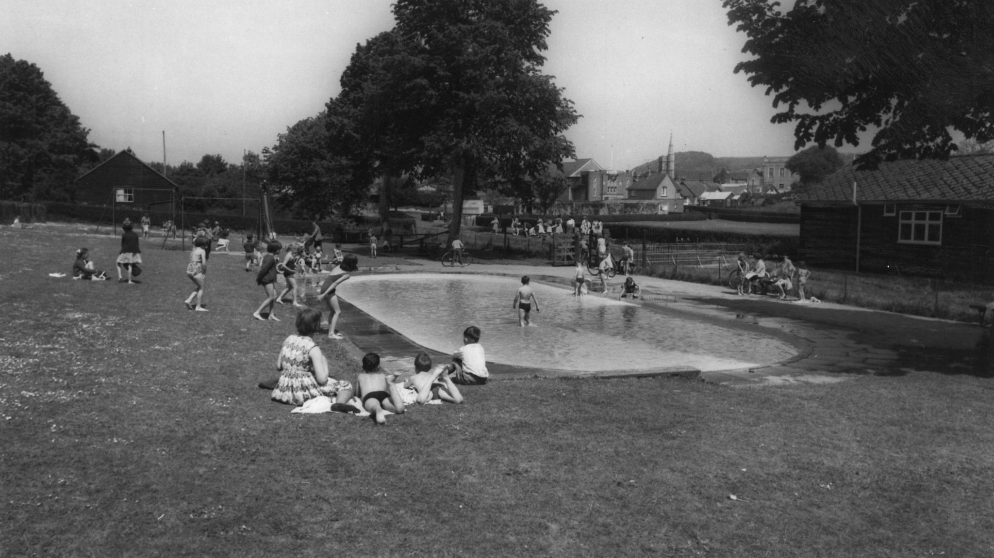 Black and white picture of a permanent paddling pool with families gathered round and a child using it