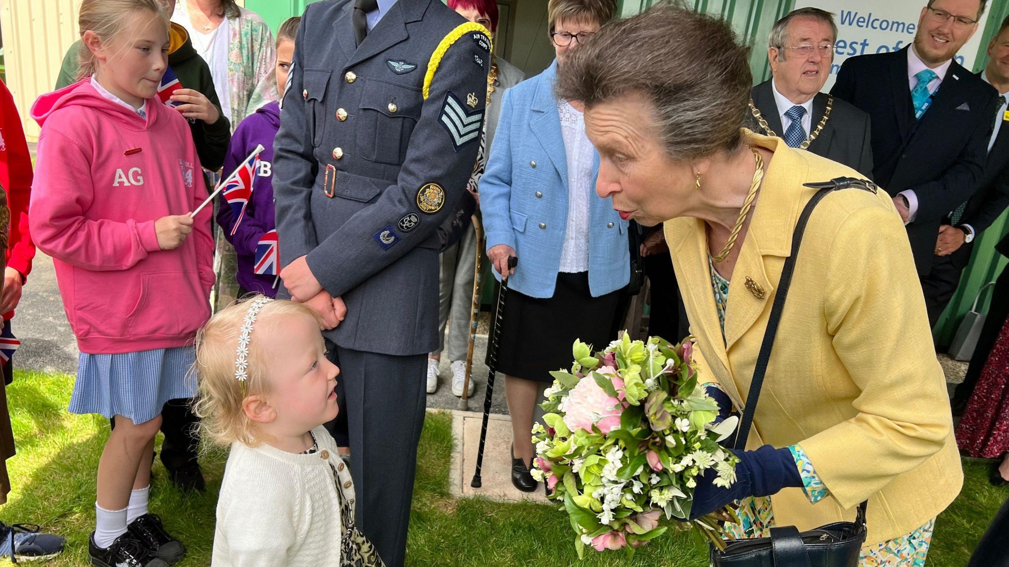 Princess Anne bending down to speak to a little girl while holding flowers