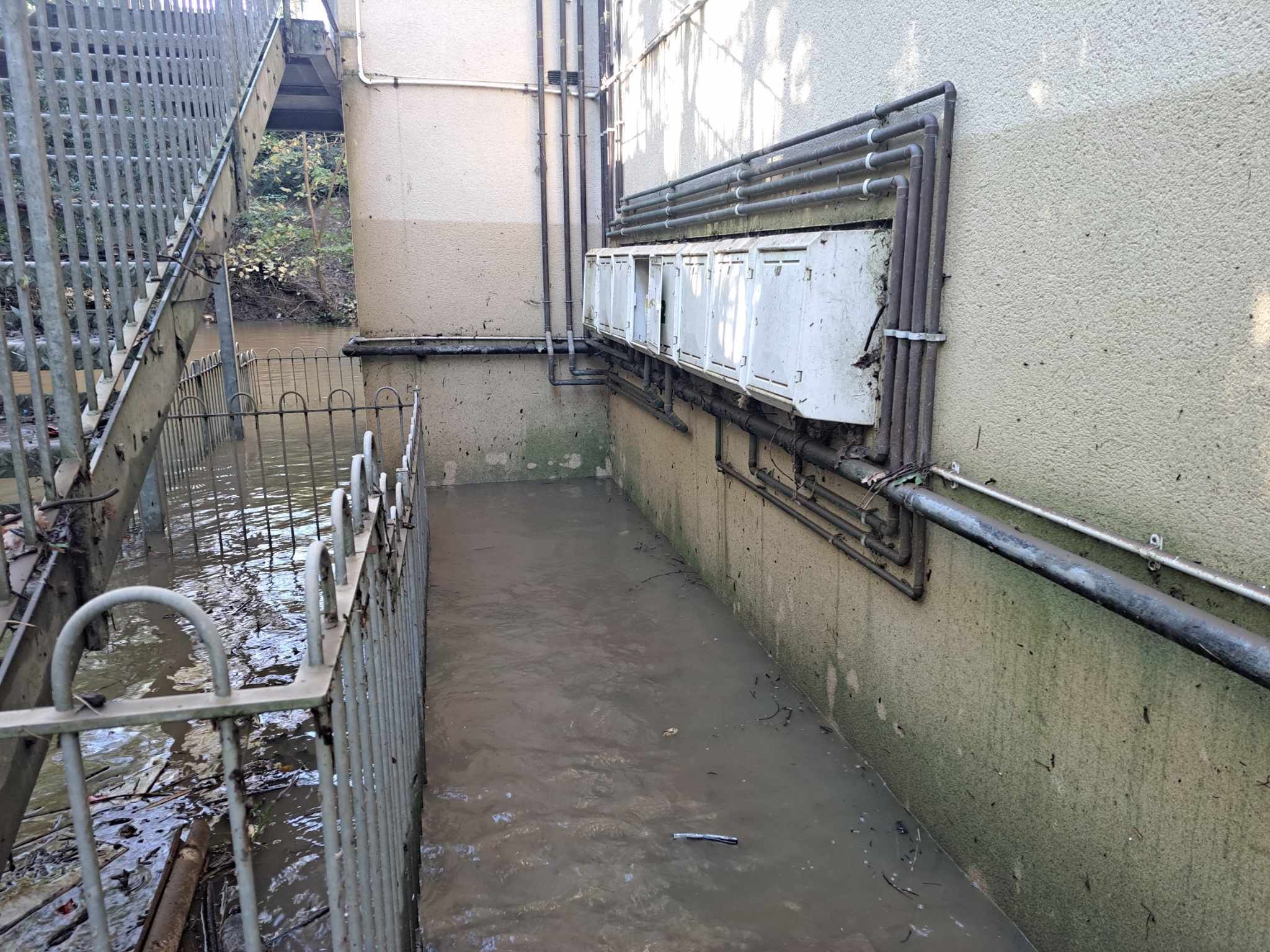 The stairwell of the block of flats, with flooding remaining and a watermark above the gas metres