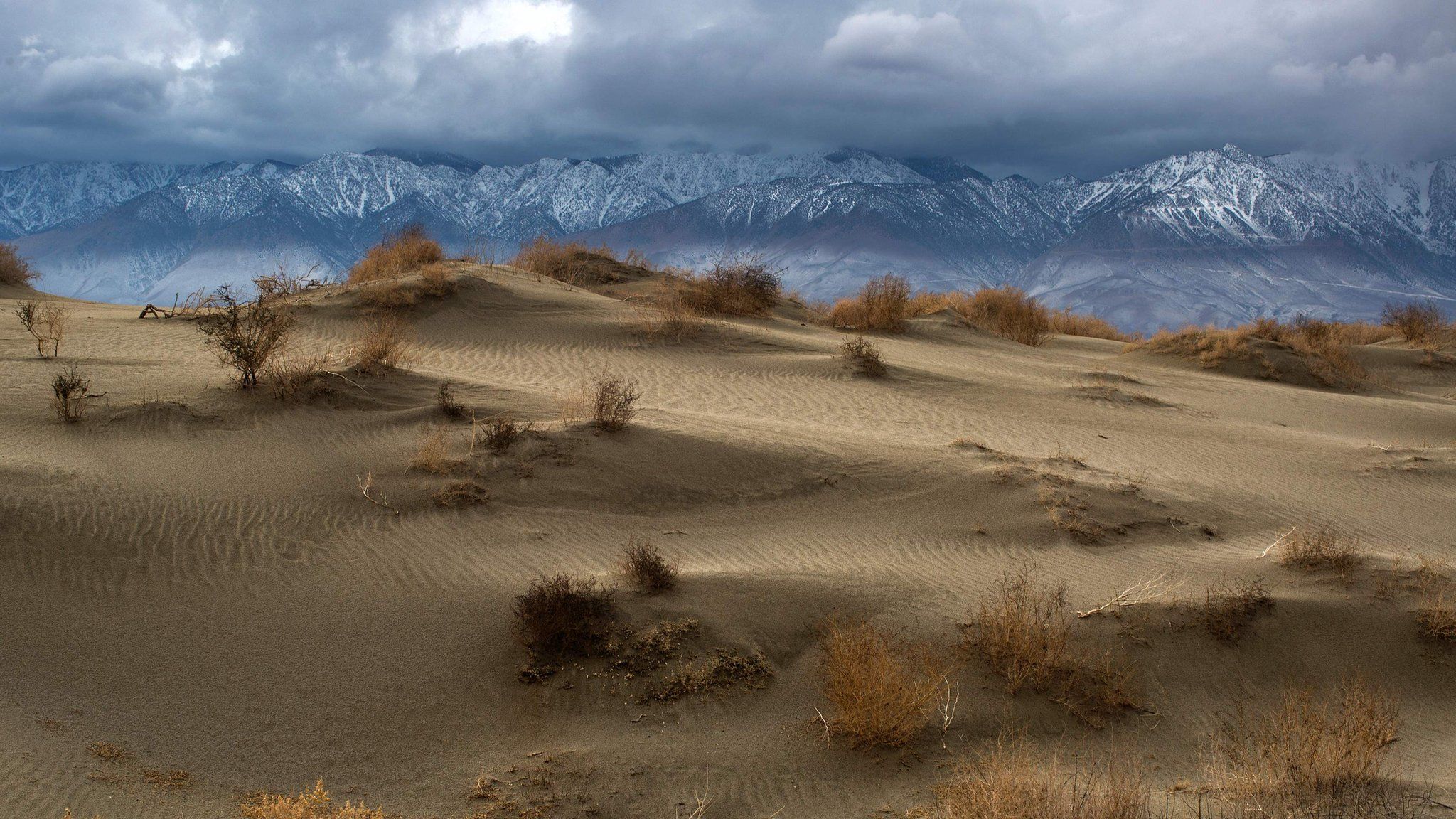 Desert sand dunes are seen with snowy Eastern Sierra Nevada Mountains in the distance near Lone Pine, California