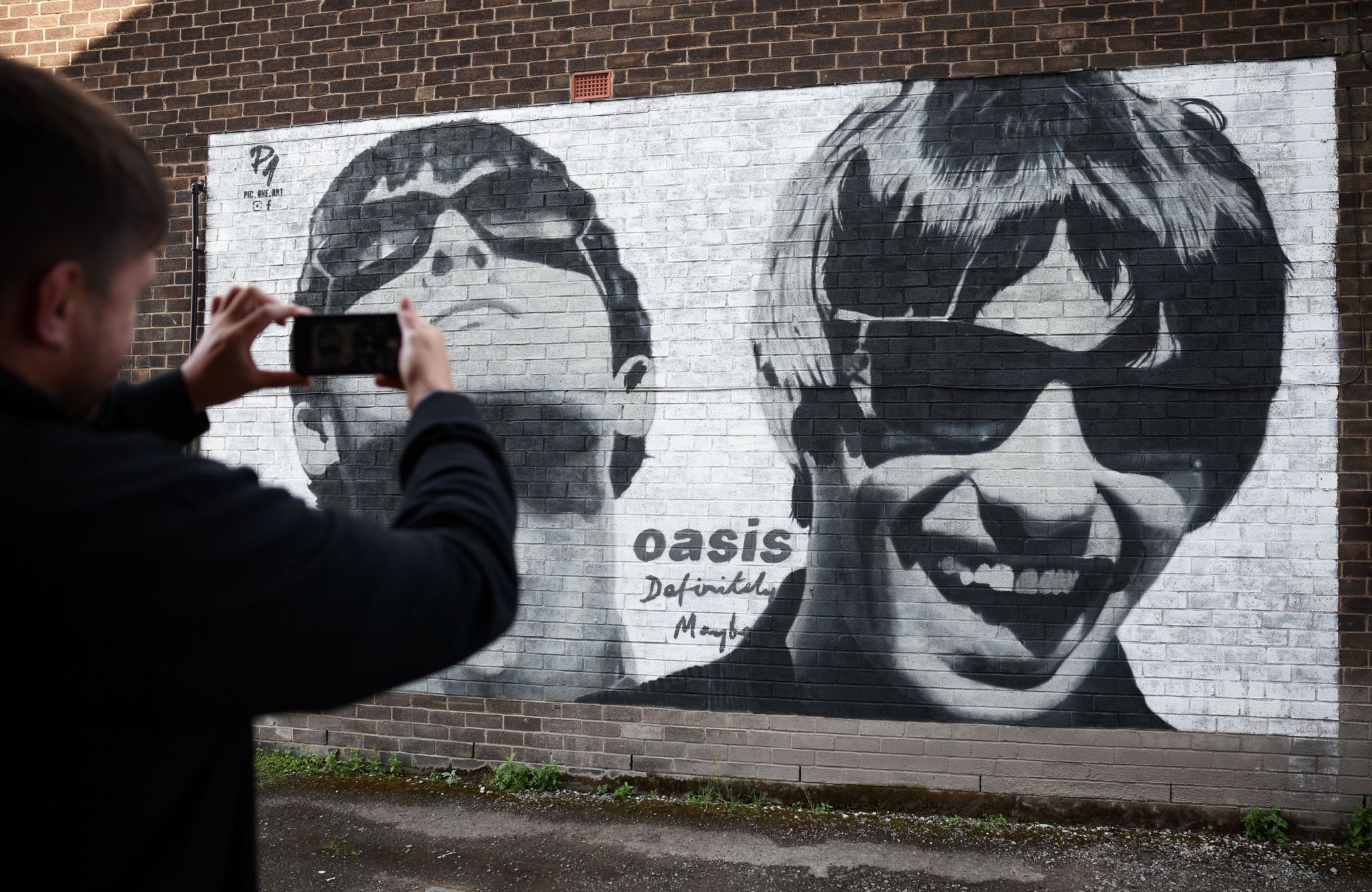 A fan photographs a mural of Liam and Noel Gallagher of British band Oasis near Sifters Records in Manchester, Britain, 29 August 2024. The mural was painted by street artist Pic.One.Art in June 2024 to mark the 30th anniversary of the band's debut album, Definitely Maybe. 