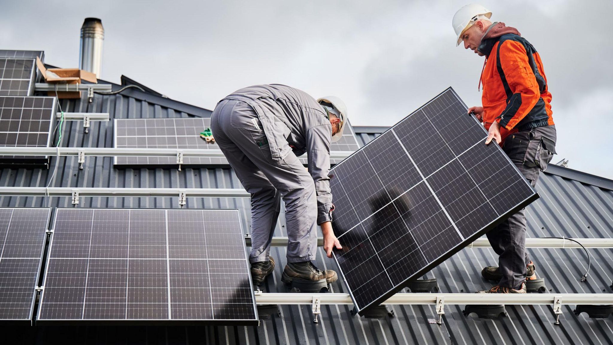 Two men work to attach solar panels to a roof