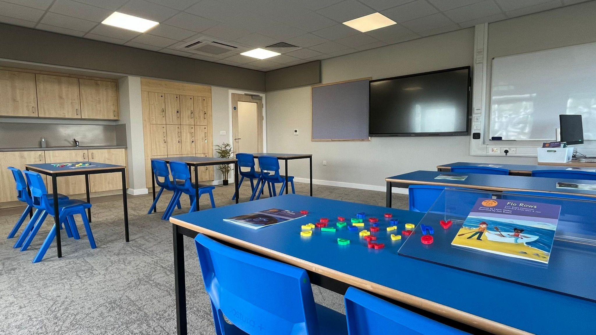 Blue tables and chairs in the new SEND hub, which also has a large television screen and whiteboard on the walls.