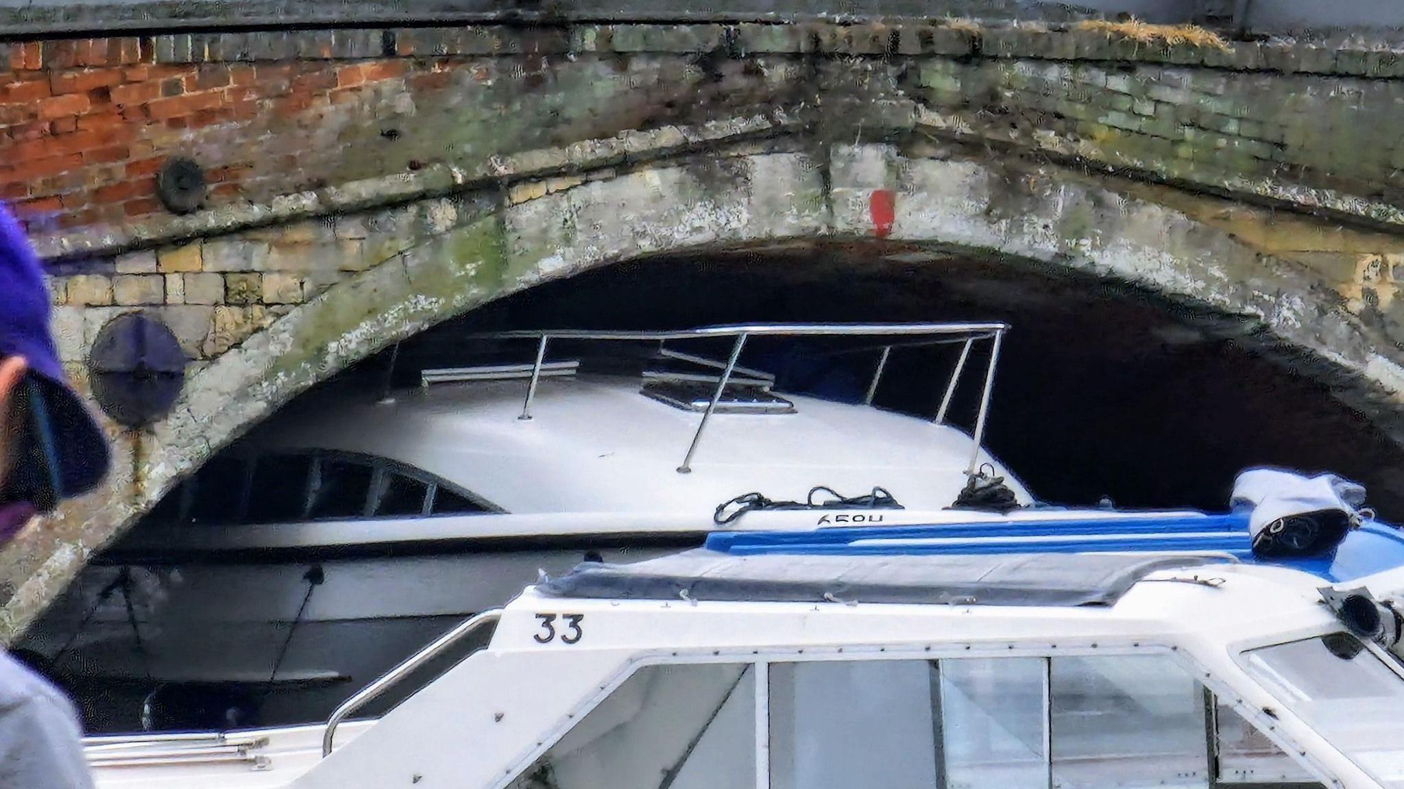 A close up of a white boat stuck under a stone bridge 