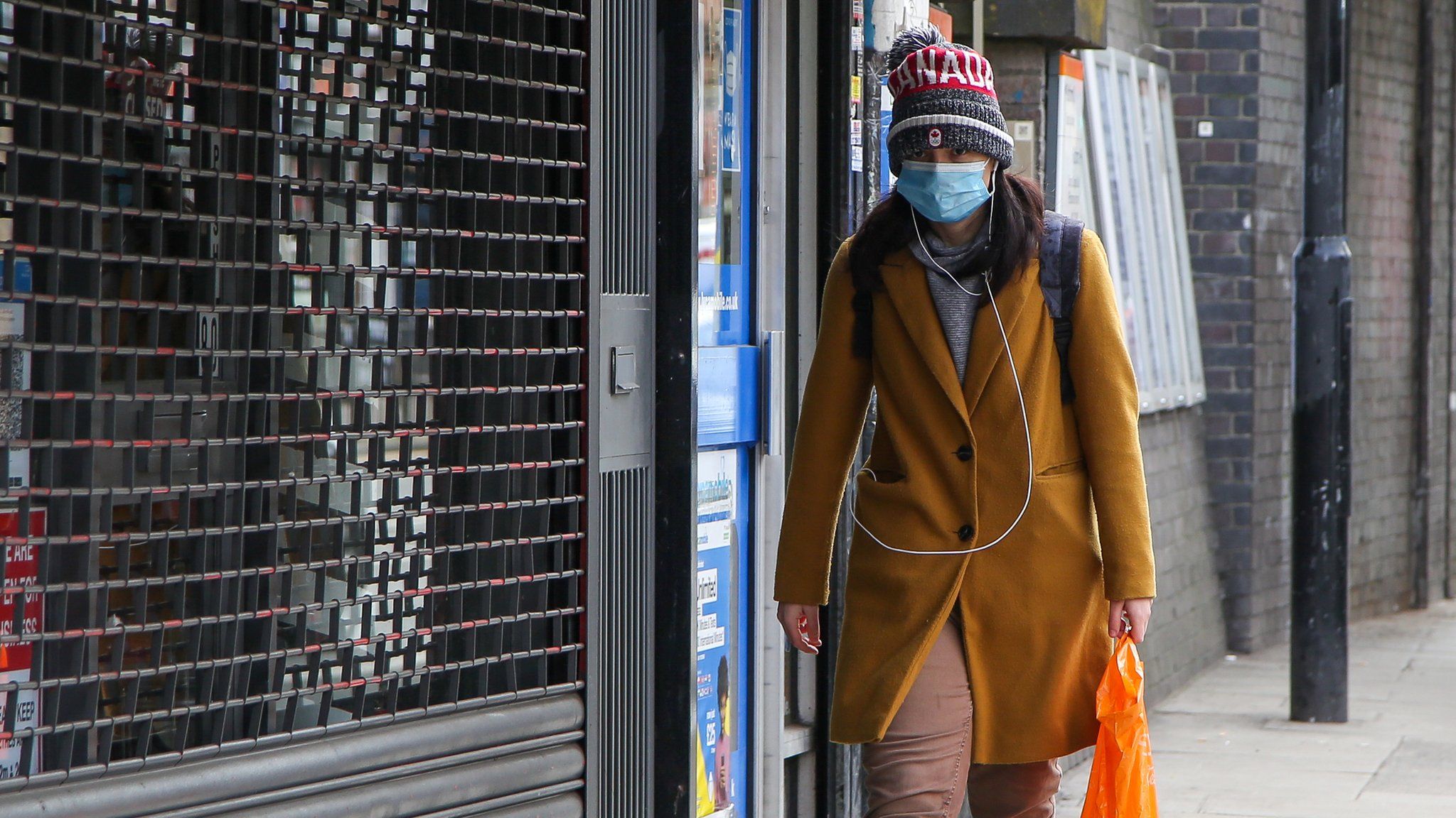 A woman wears a face covering while walking down a street in London