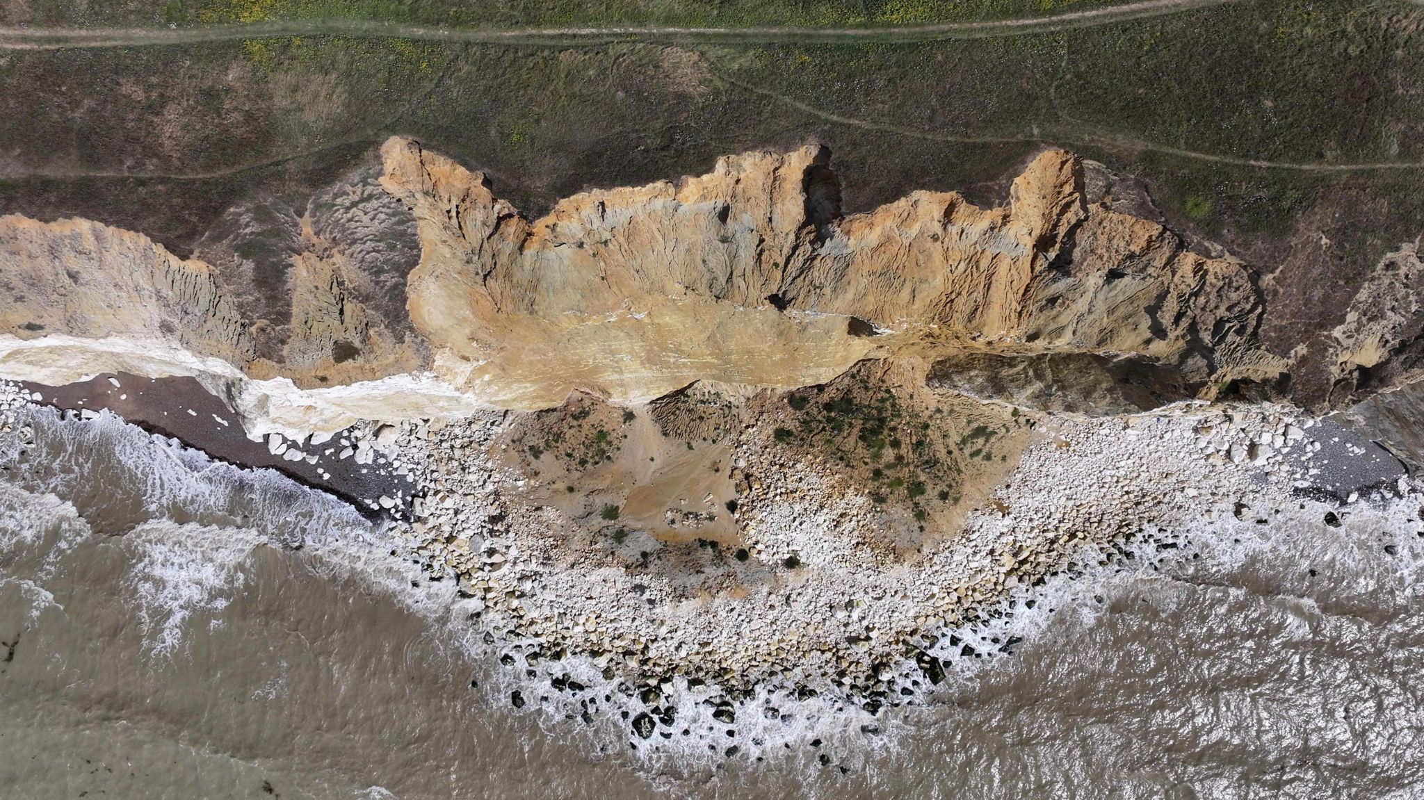 A drone shot directly above the cliff fall, looking down on the debris by the ocean