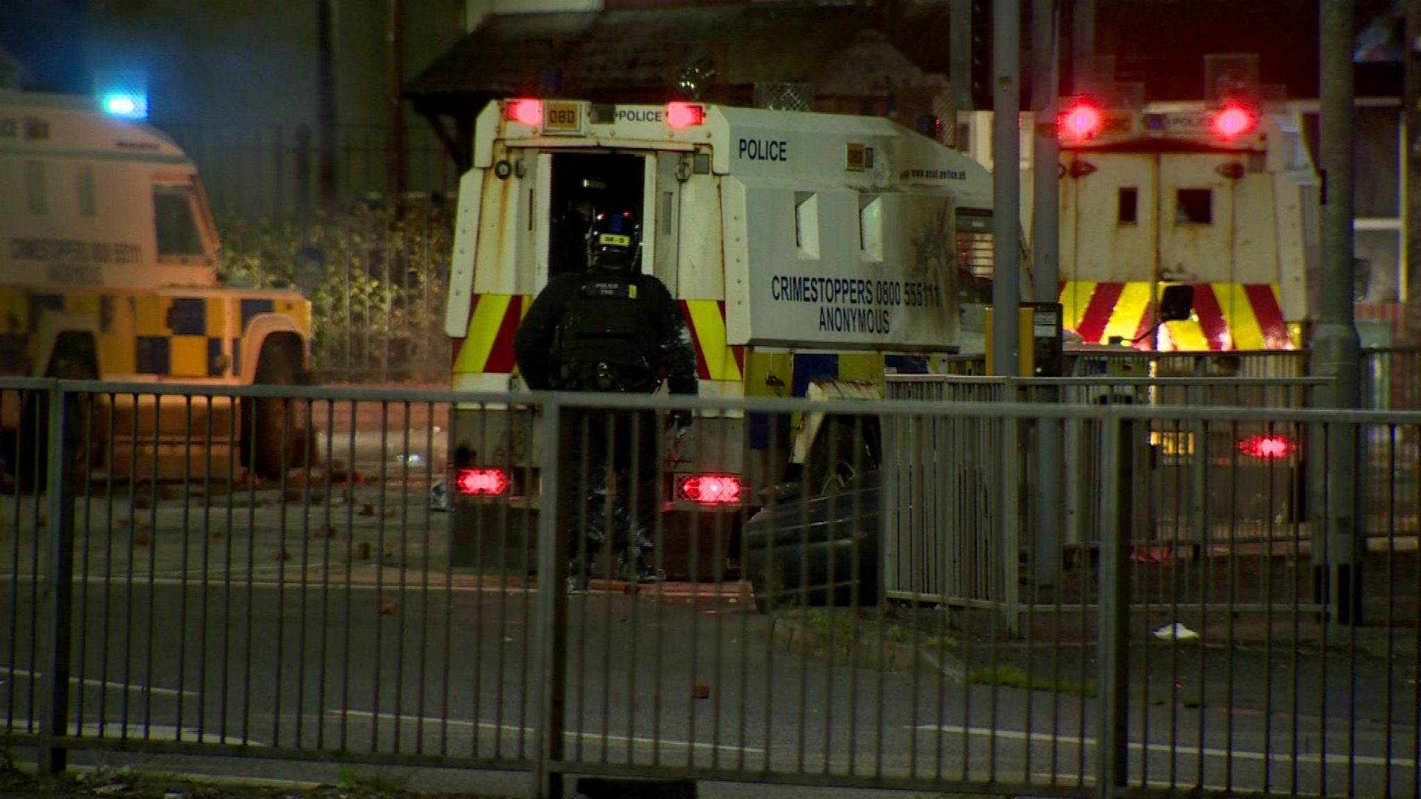 Police officer in riot gear stands at the open back door of a land rover during the violence