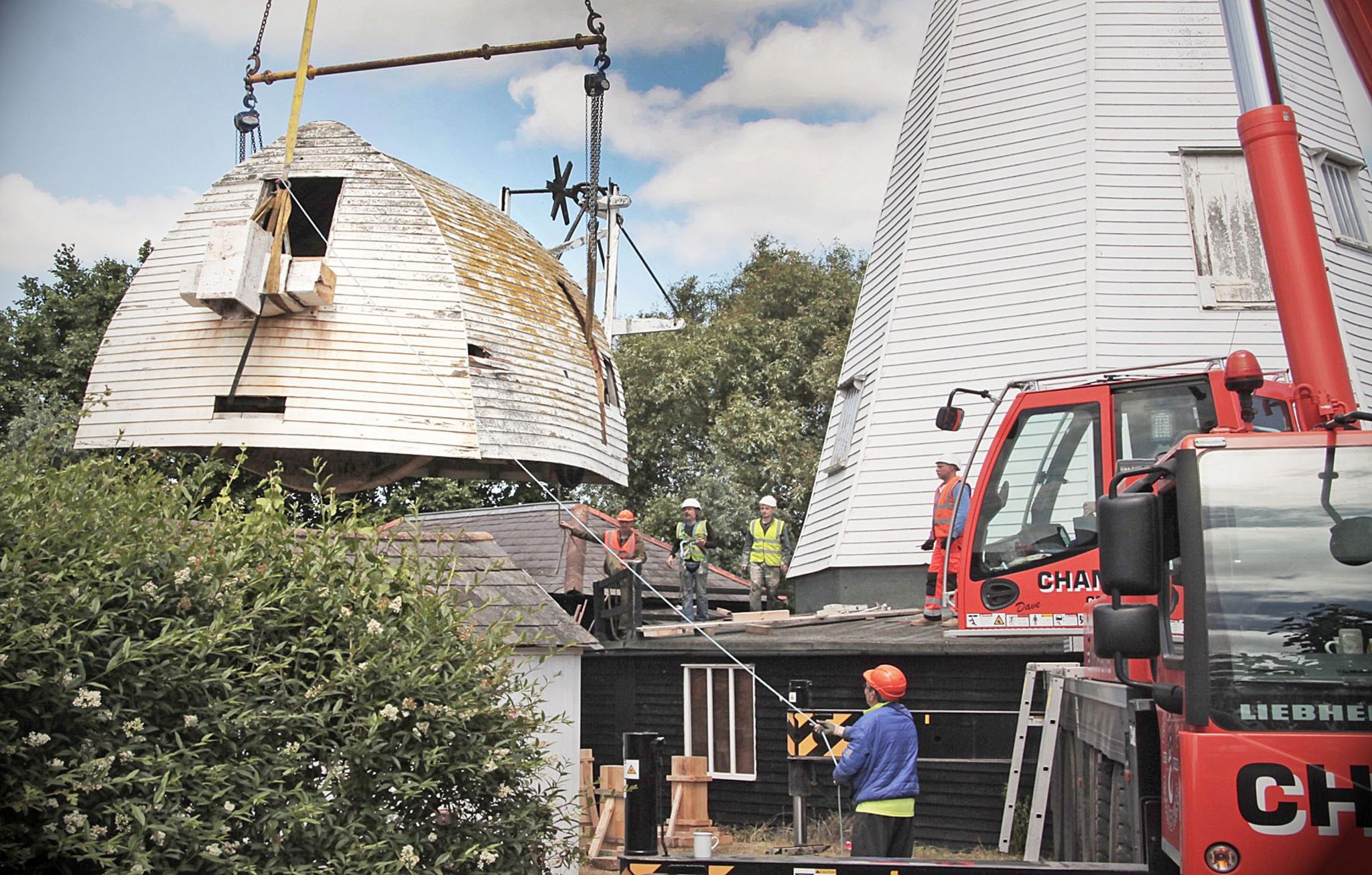 Volunteers guide a windmill cap to the ground with the help of a crane